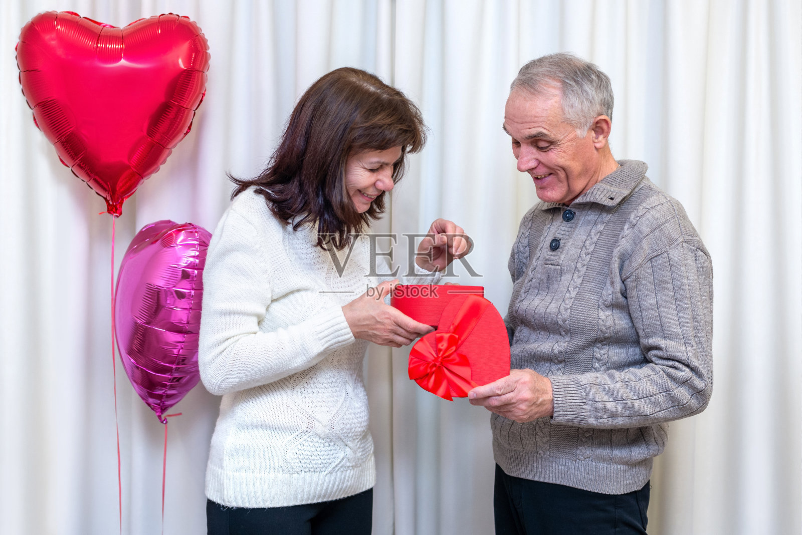 快乐的老夫妇庆祝情人节。男人送给女人一个心形的礼盒。浪漫的关系，退休后的爱情和约会。老年人的生活方式。成熟的退休人员。照片摄影图片