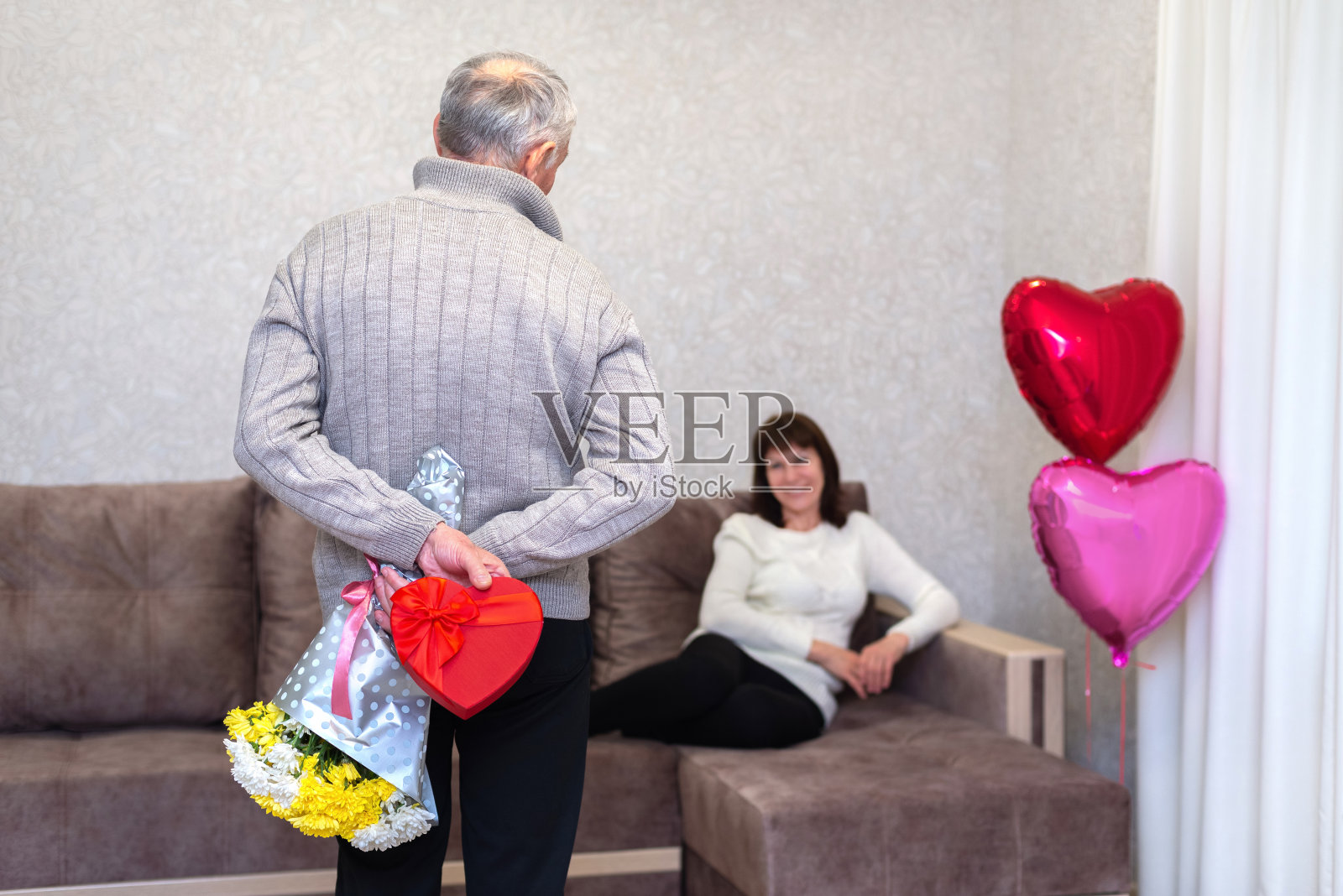 快乐的老夫妇庆祝情人节。男人背后拿着礼物和鲜花。恋爱，爱情，退休后约会。老年人的生活方式。成熟的退休人员。照片摄影图片