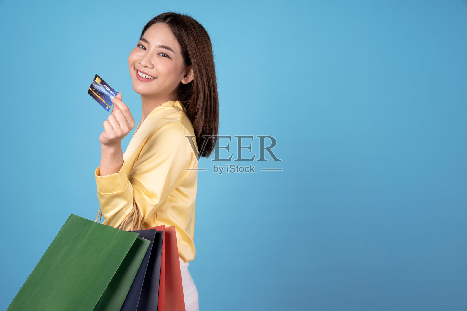 快乐的亚洲女人拿着购物袋在五颜六色的蓝色背景。照片摄影图片