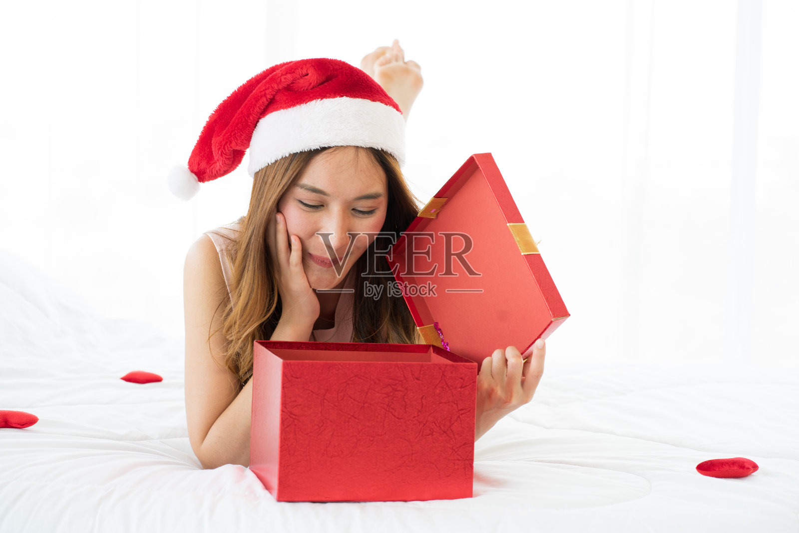 亚洲美丽迷人的年轻女子戴着圣诞老人的帽子在床上电传有美好的时间在圣诞节节日期间在家照片摄影图片