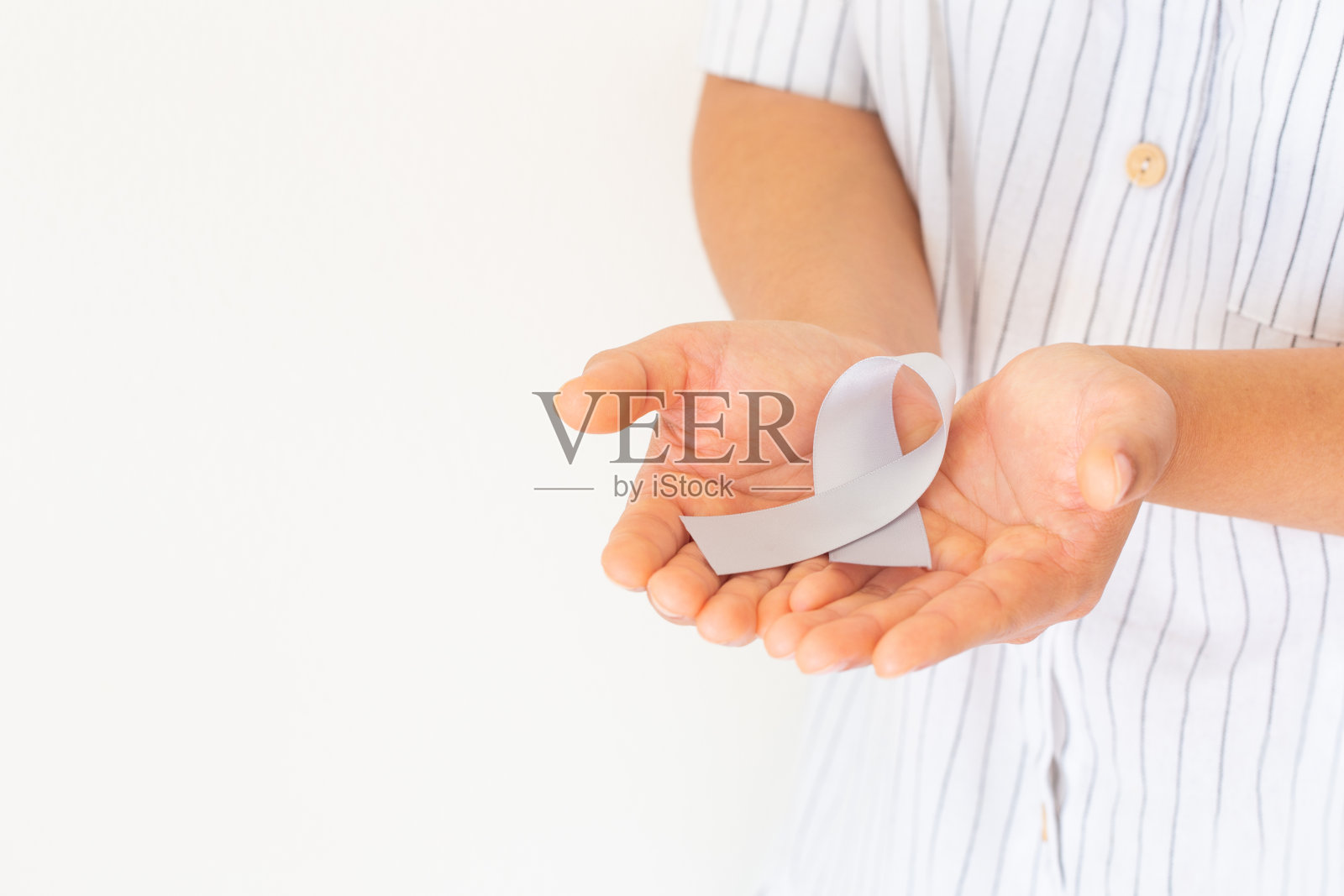 手拿灰色的丝带在白色的背景。采购产品脑癌意识，脑肿瘤，过敏，哮喘，糖尿病意识，失语症，精神疾病。医疗保健医疗的概念。照片摄影图片