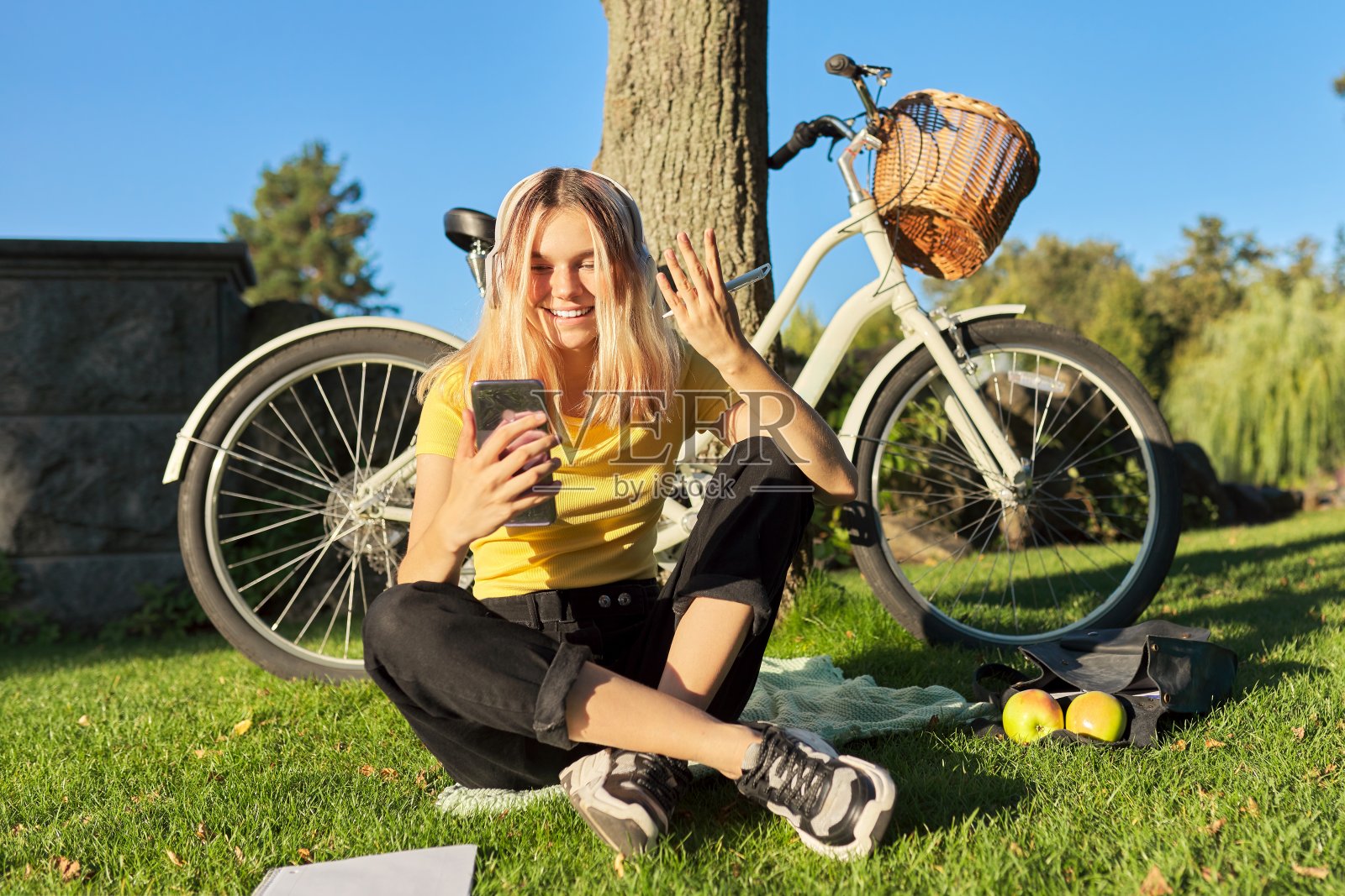 戴着耳机骑着智能手机的青少年学生坐在公园里照片摄影图片
