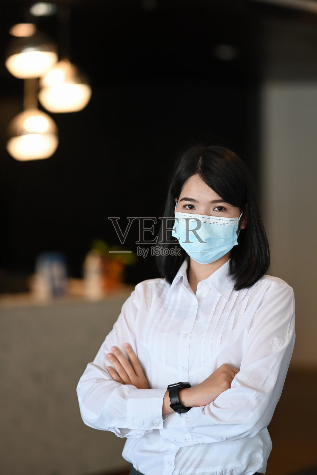 自信的女商人戴着防护面具，双手交叉站在现代办公室里的肖像。照片摄影图片