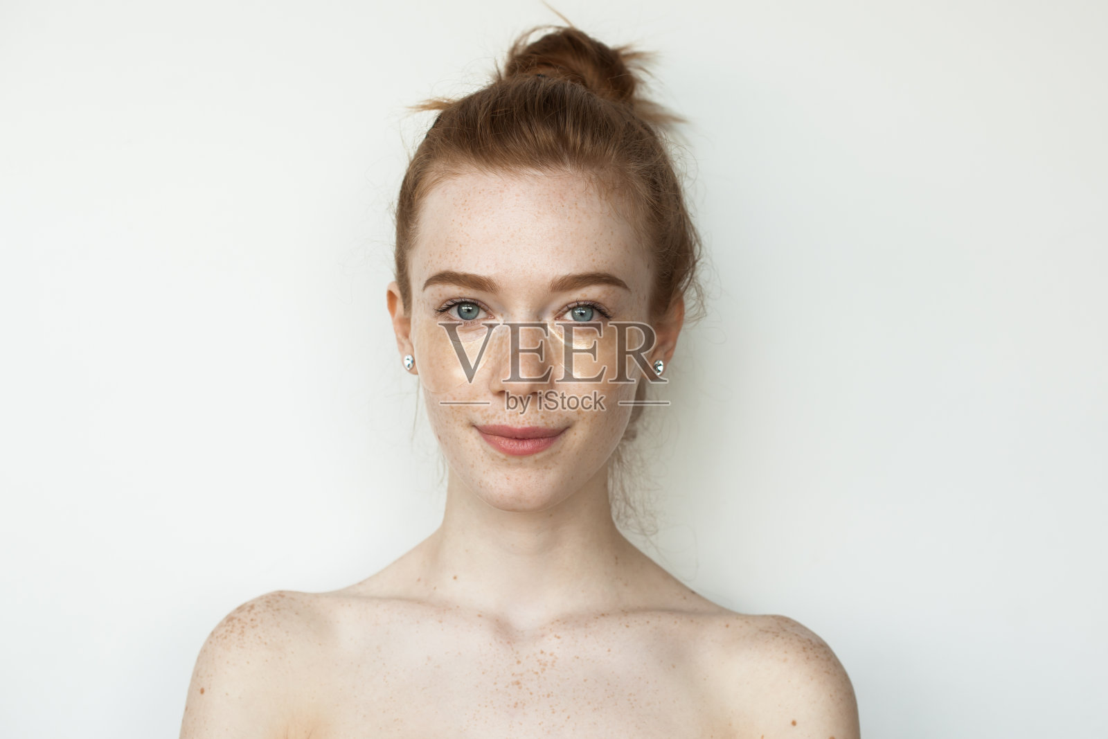 一名长着雀斑、红头发的白种人女子戴着水凝胶眼罩，裸肩站在一面墙上照片摄影图片