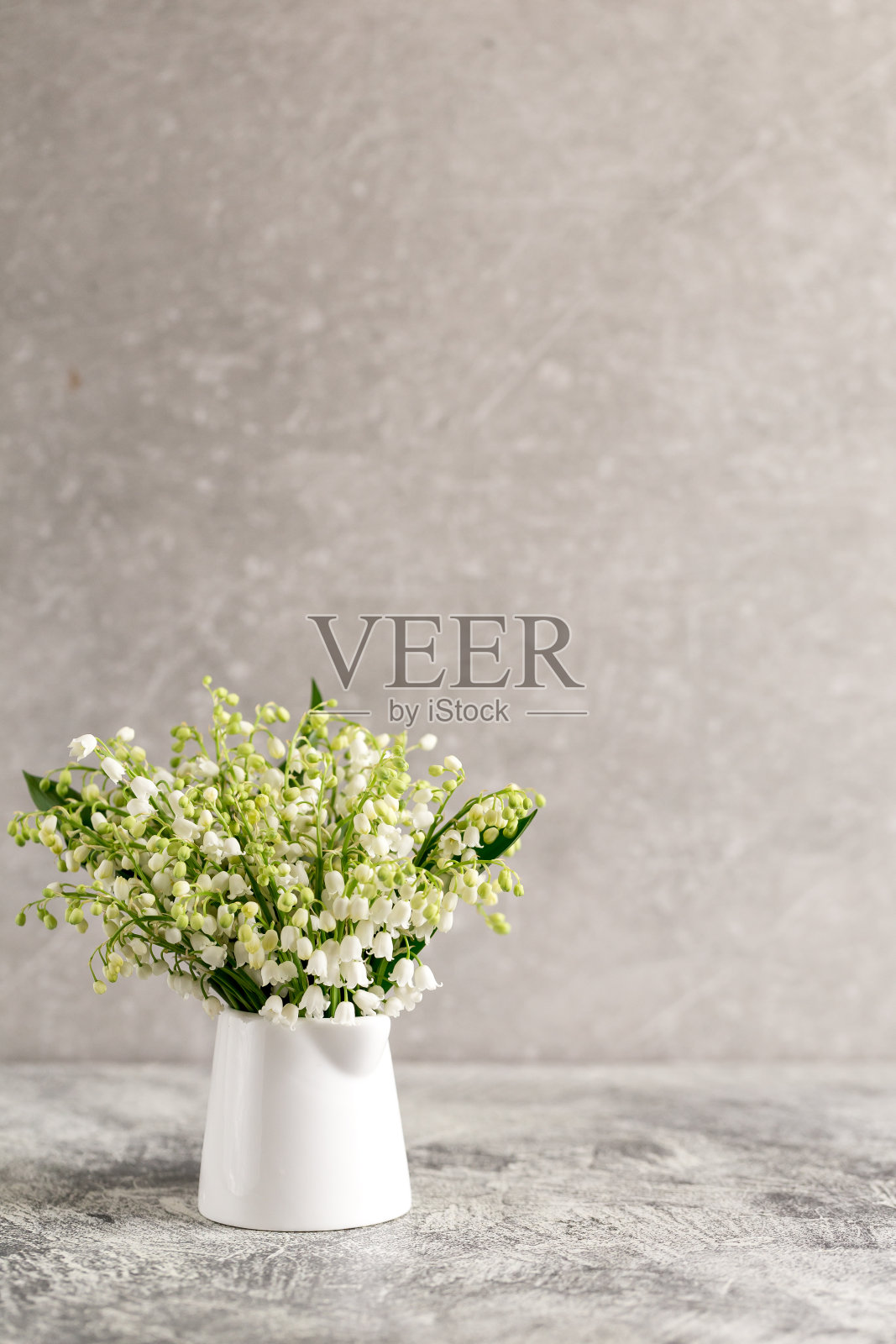 在灰色的混凝土背景下，白色的玻璃里放着山谷百合的花束照片摄影图片