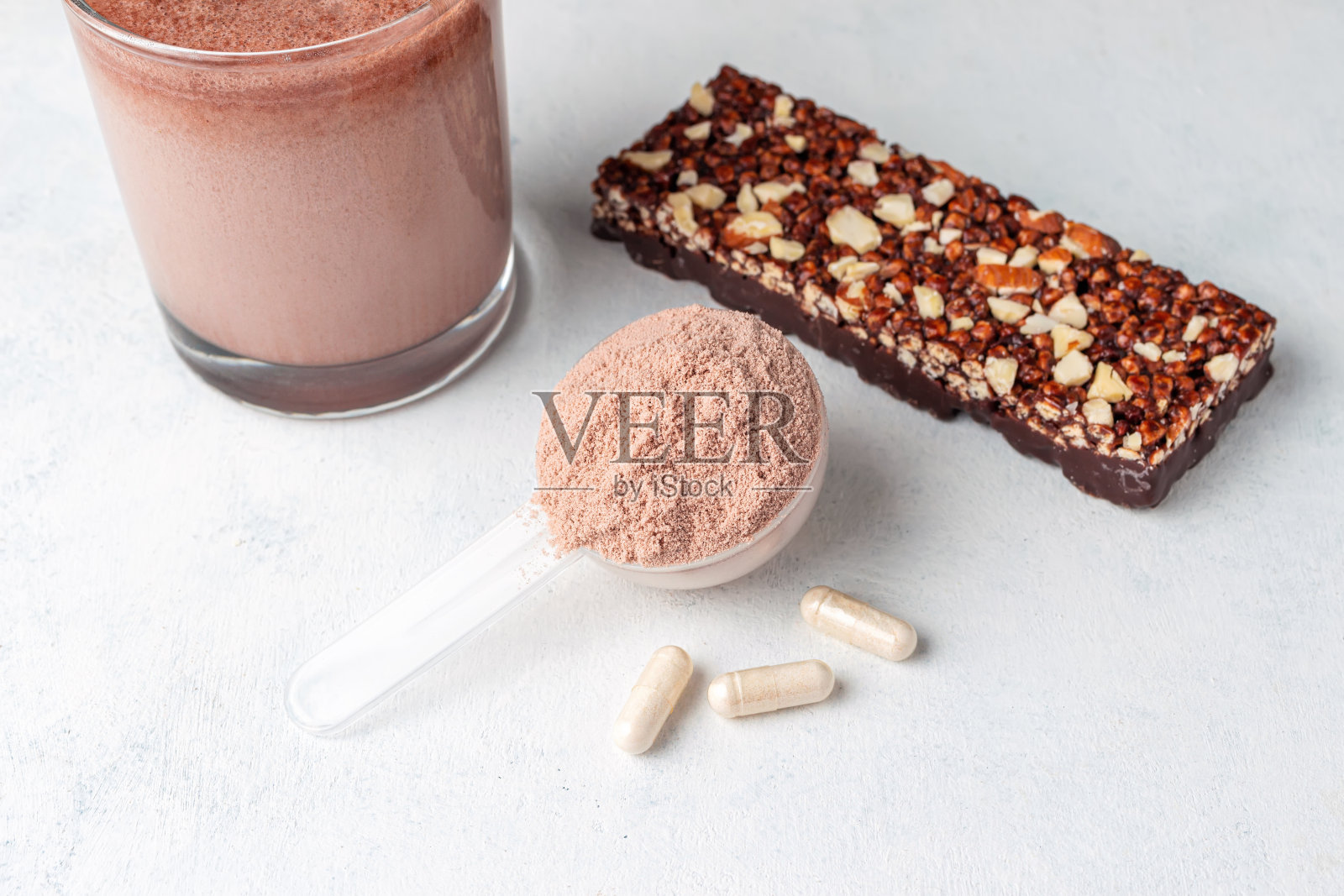 一勺乳清分离蛋白，一杯巧克力奶昔，格兰诺拉燕麦棒，氨基酸和肌酸的白色胶囊，在白色桌子背景上的健身食品补充剂照片摄影图片