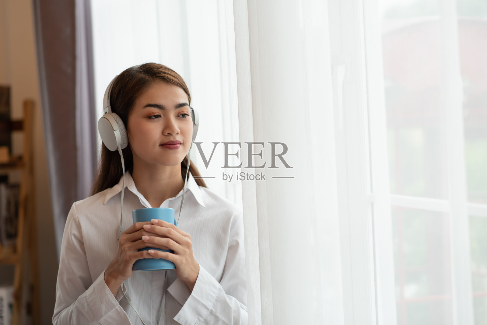 年轻的亚洲女子喜欢戴着耳机听音乐，捧着一杯热咖啡，快乐和放松的时光照片摄影图片