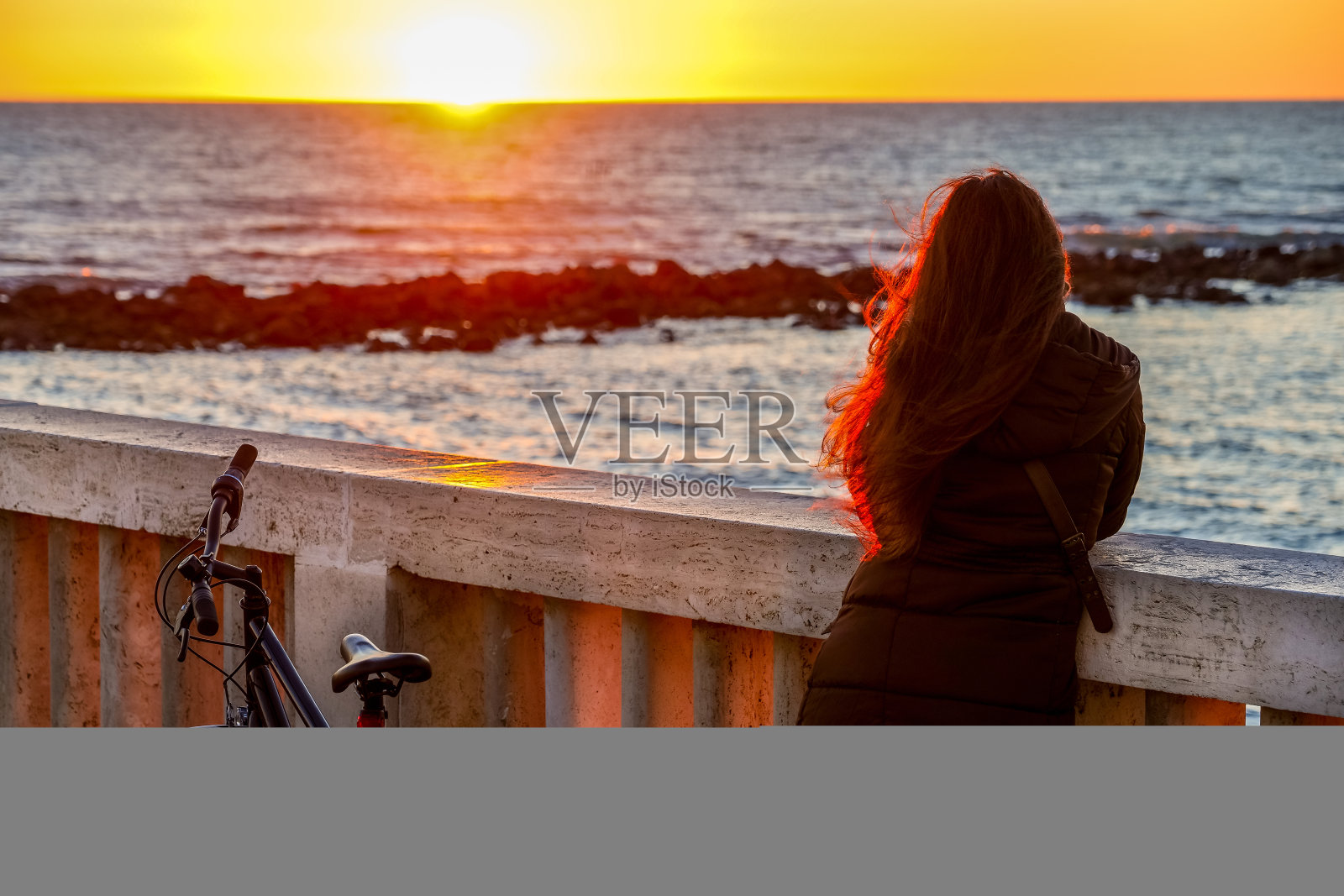 一个长发女子在欣赏一个浪漫的日落在海上-高清图像照片摄影图片