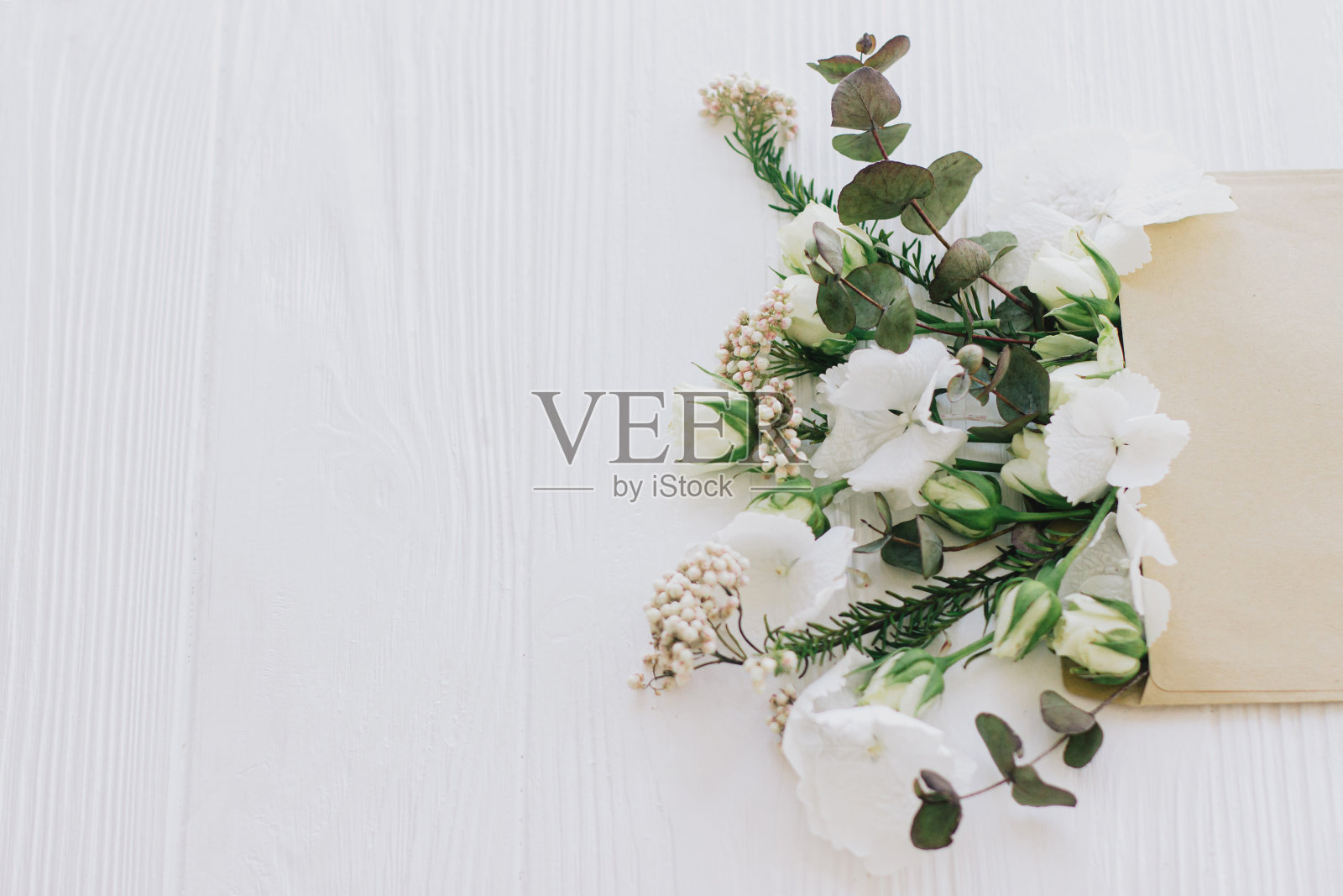 玫瑰，绣球花和桉树的树枝从工艺信封上生长在白色的木材，复制空间照片摄影图片