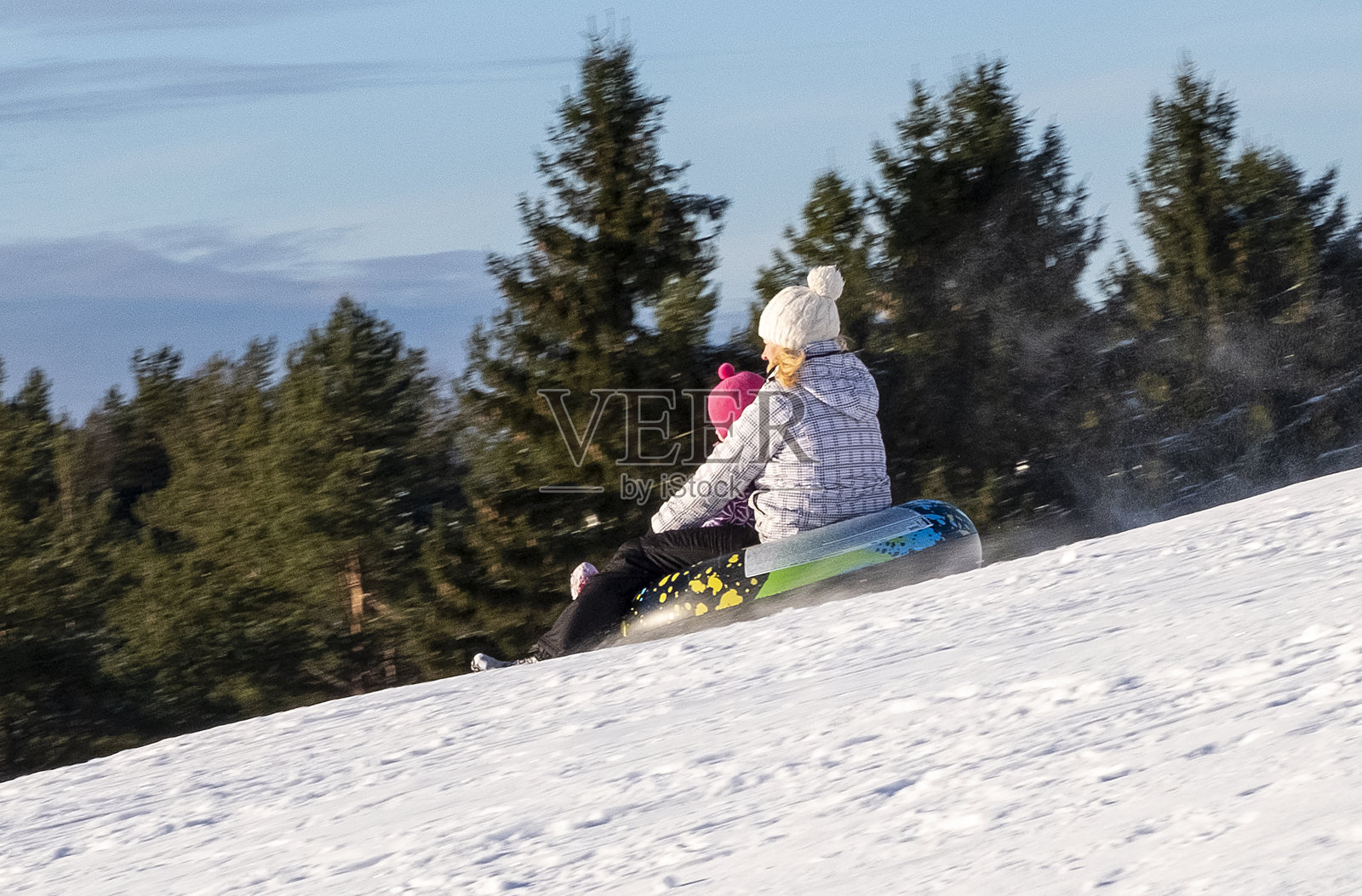 家人在冬天度假。一名妇女和一个5岁的白种人孩子，在一个充气滑梯上快速滑下一个覆盖着积雪的滑梯。照片摄影图片