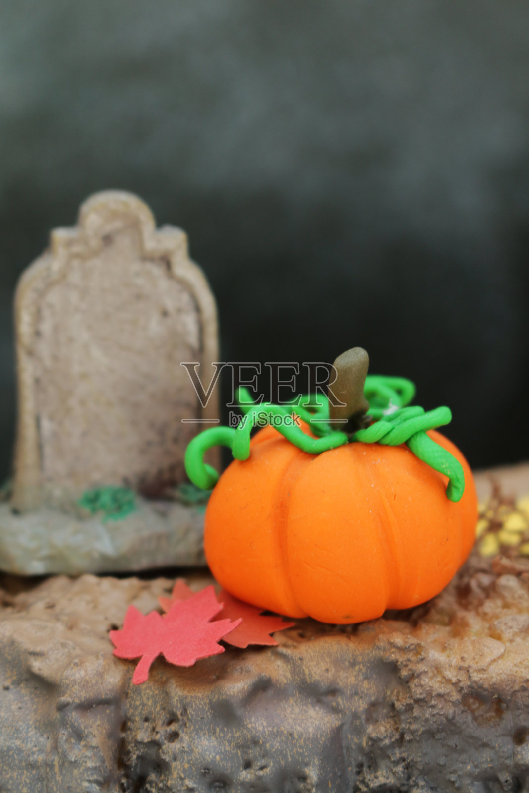 特写图像的模型万圣节场景与一个自制的模型粘土南瓜旁边的微型墓碑和秋天的彩色纸叶子，季节性的节日概念照片摄影图片