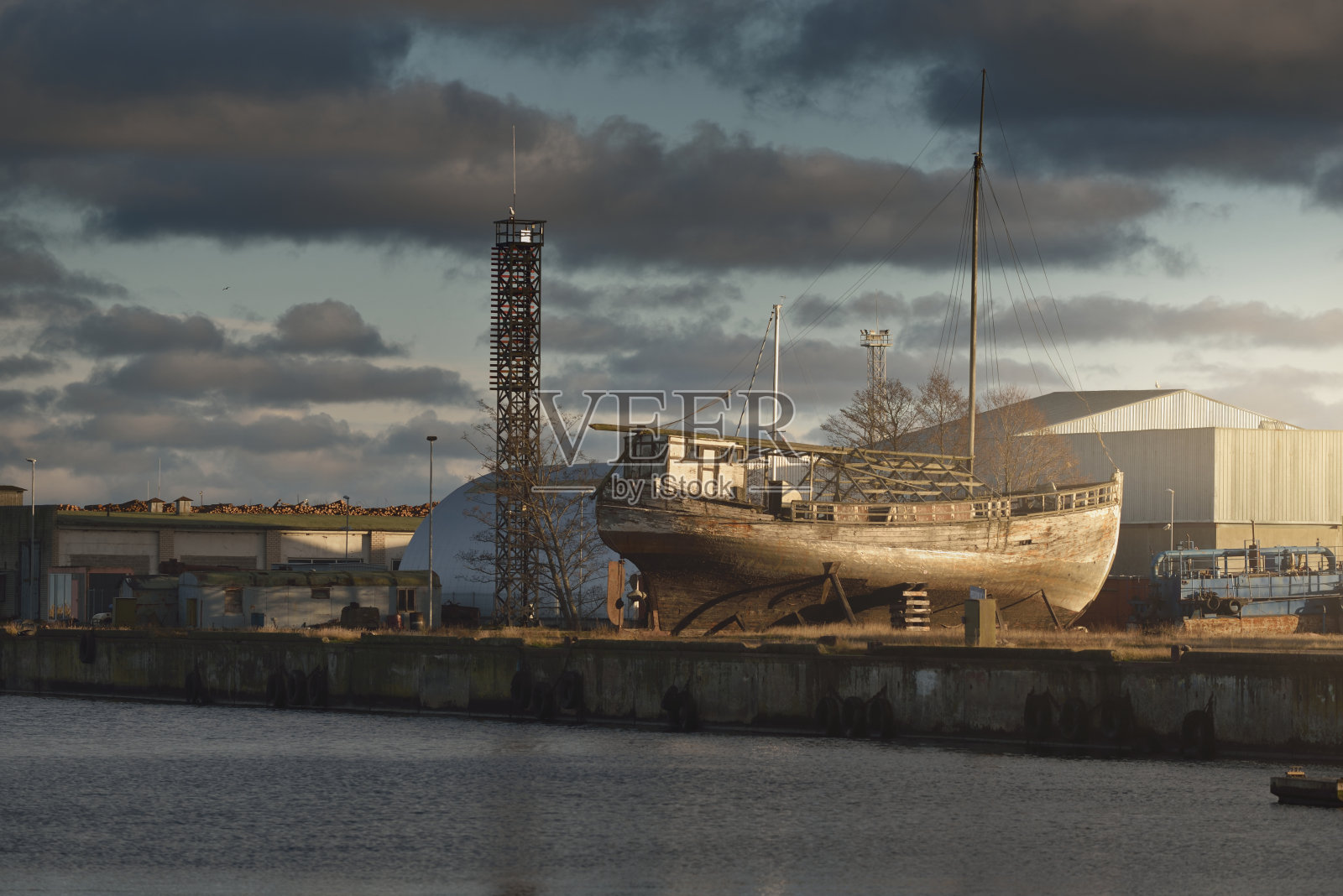 日落时分停泊在港口陆地上的旧木船(渔船)。波罗的海,拉脱维亚。柔和的阳光，引人注目的天空。工业，商业，运输，服务，物流，航运，历史，过去照片摄影图片