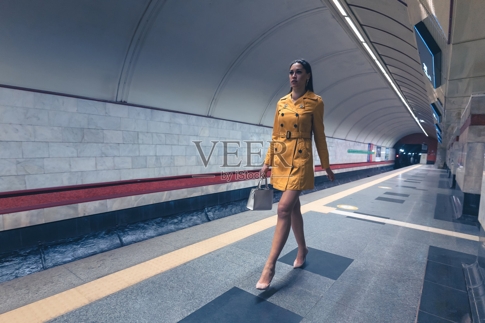 走在地铁站台上的漂亮女孩长腿，穿着黄色的春装，手里拿着白色的手提包或钱包照片摄影图片