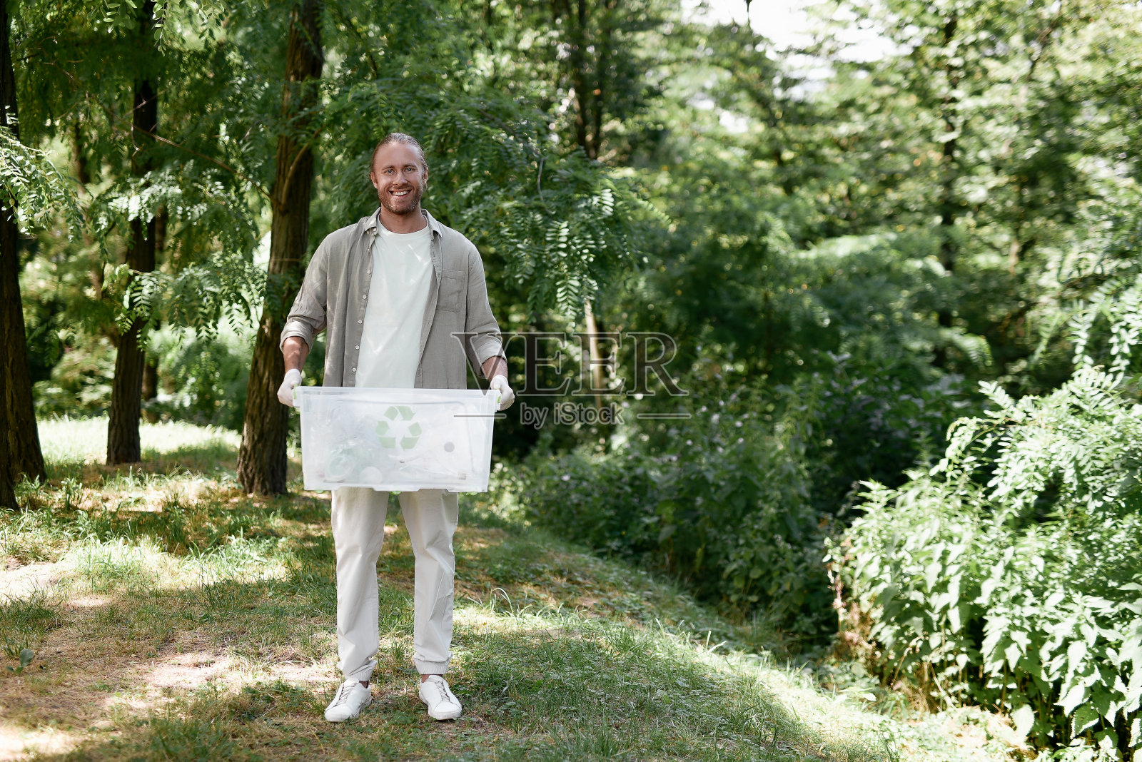 志愿服务的概念。年轻快乐的生态活动家在森林或公园收集塑料，拿着回收箱，对着镜头微笑照片摄影图片
