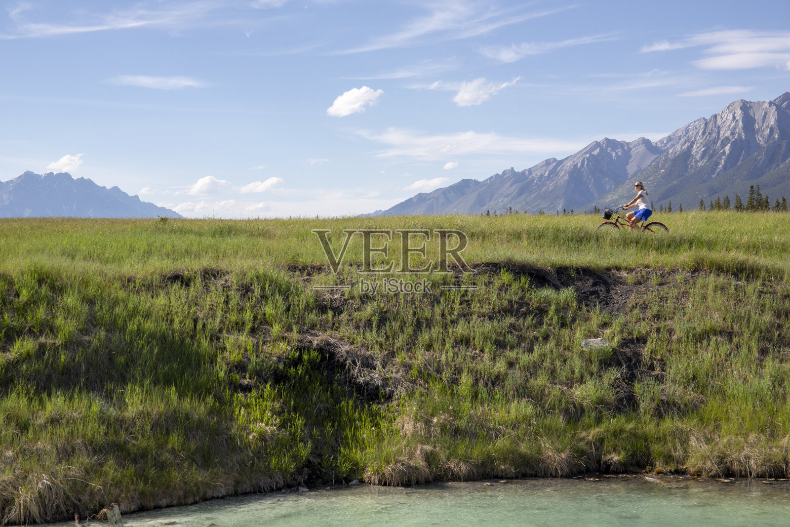 远处，一个女人骑着一辆巡洋舰自行车穿过山区的草地照片摄影图片