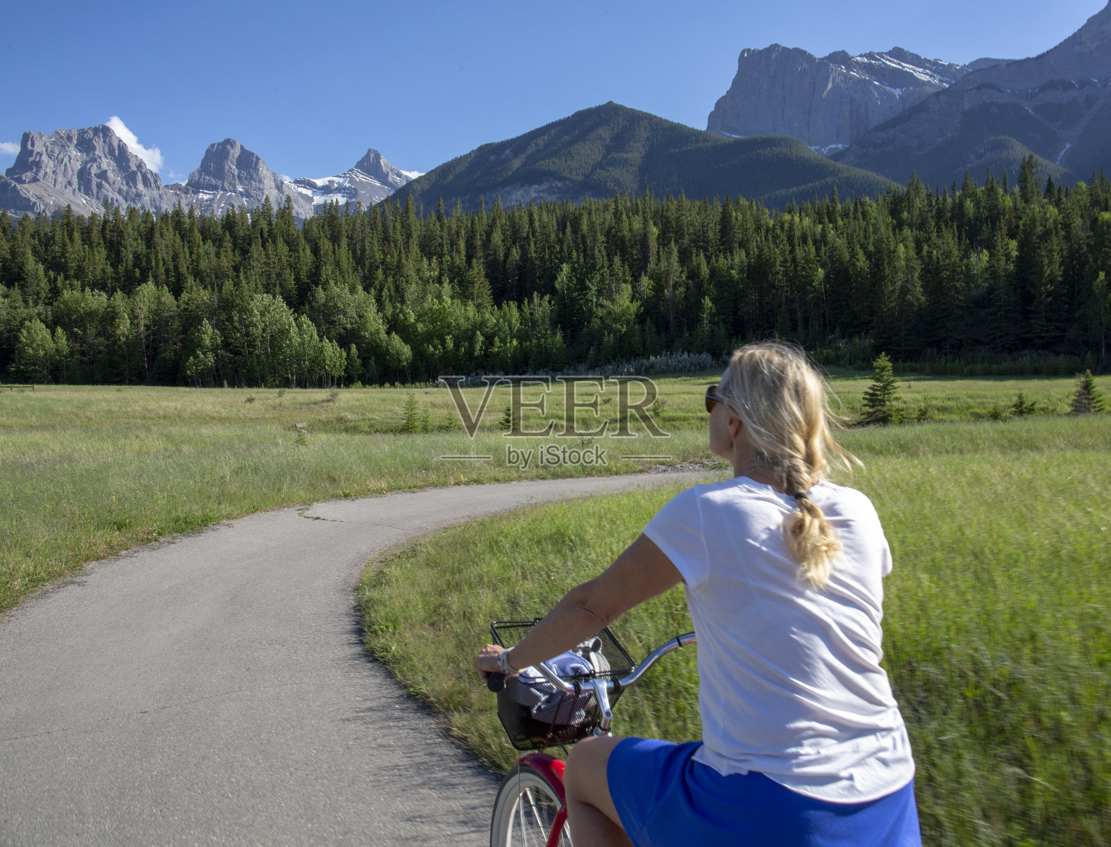 一名女子骑着一辆巡洋车，沿着蜿蜒的小路穿过山区的草地照片摄影图片