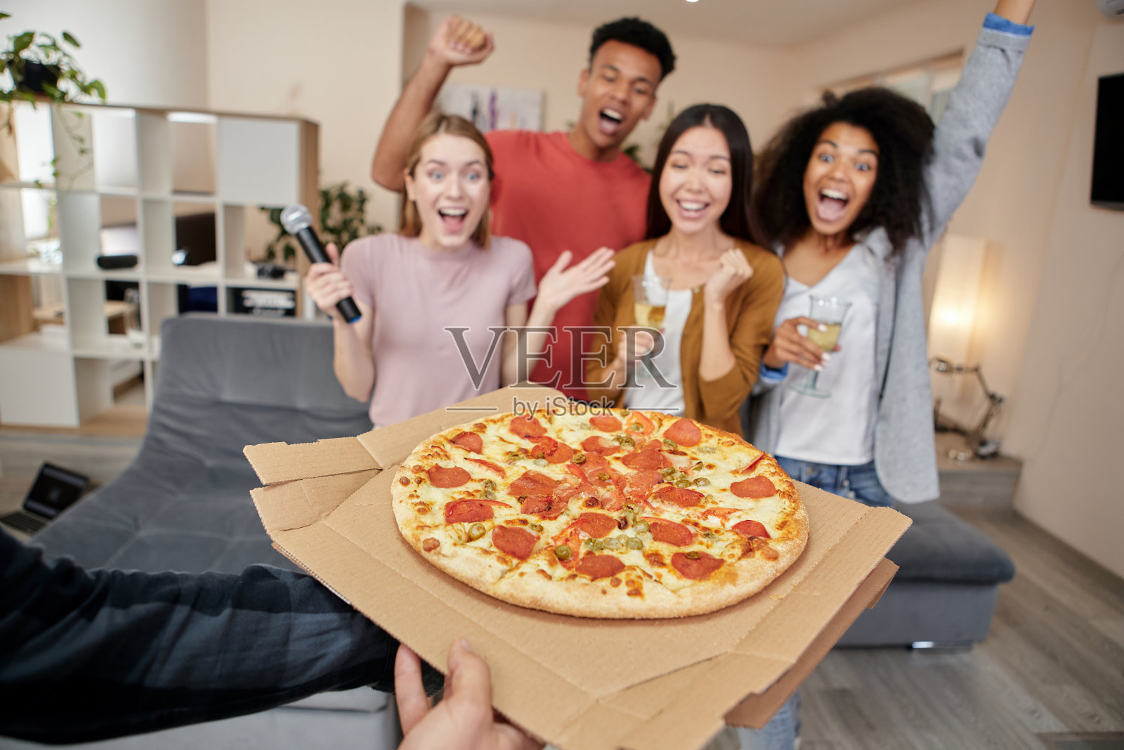 美味的披萨。兴奋的来自不同文化背景的朋友们一边在现代公寓里开卡拉ok派对，一边拿着麦克风唱歌，一边享用新鲜出炉的披萨照片摄影图片