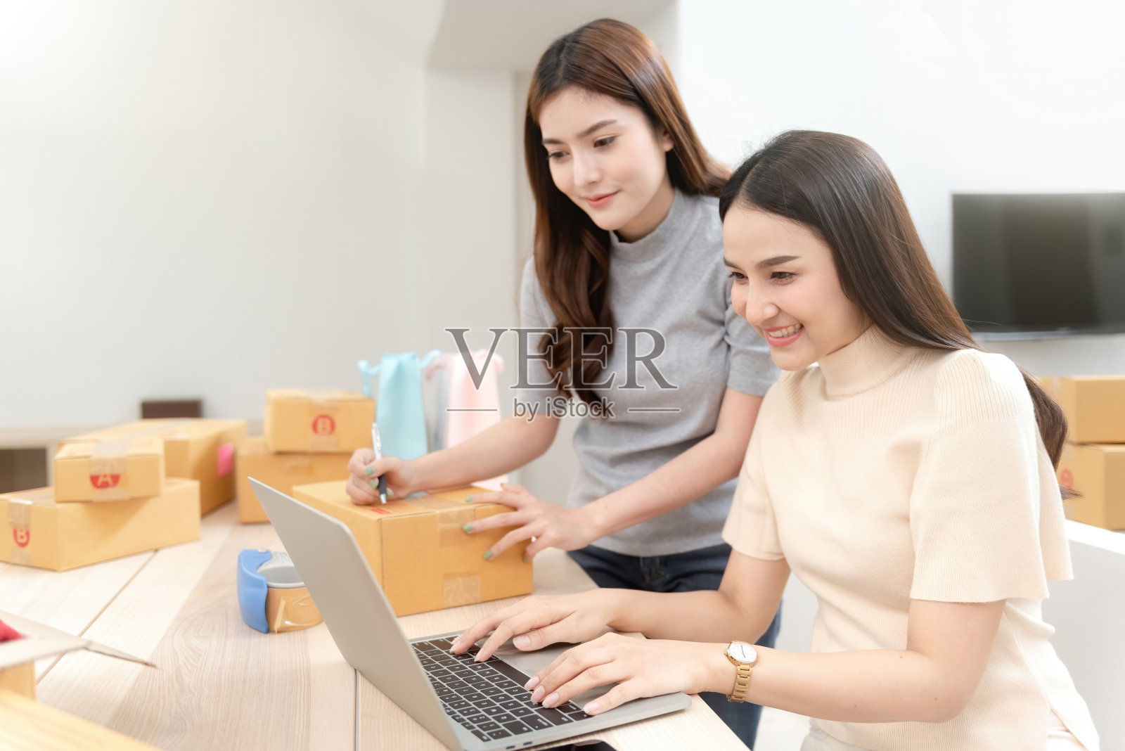 两位美丽的亚洲女性正在网上用笔记本电脑查看订单。用快乐的笑脸包装纸盒，成为网上新常态照片摄影图片