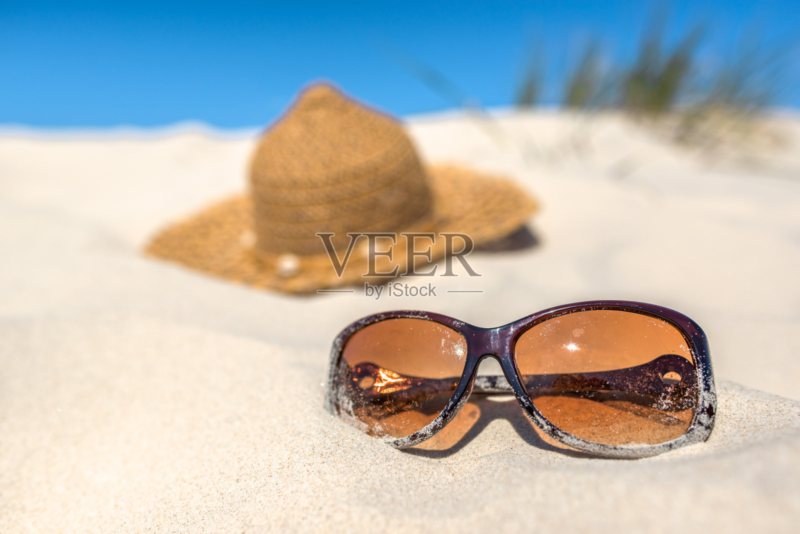 背景与夏季度假配件在海滩上，太阳镜和太阳帽在沙丘和蓝天。照片摄影图片