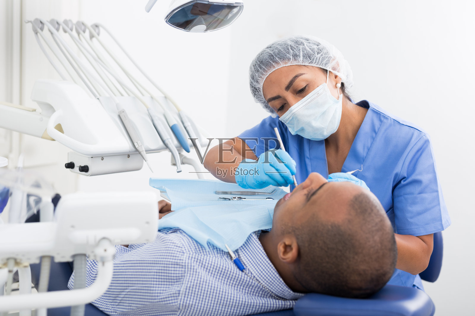 穿制服的牙医正在检查椅子上的人照片摄影图片