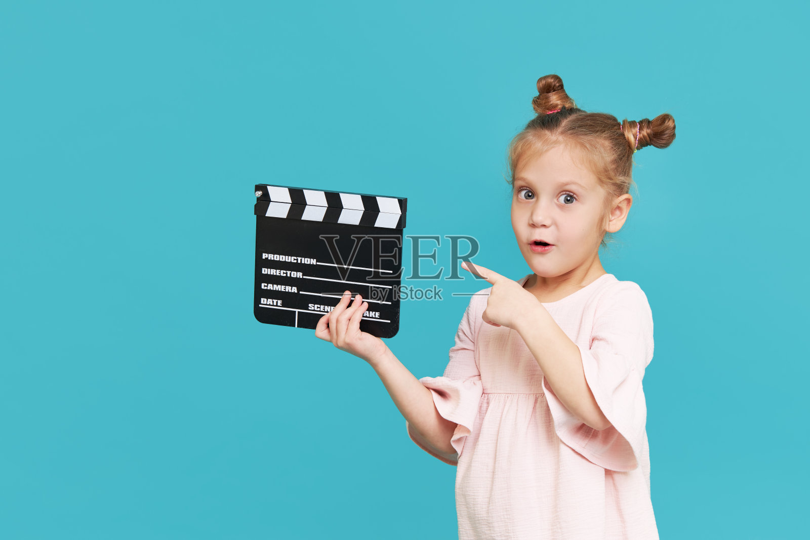 滑稽微笑的小女孩拿着电影制作板孤立在蓝色的背景。小剪匠，表演训练。有趣的脸。为文本复制空间。“t照片摄影图片