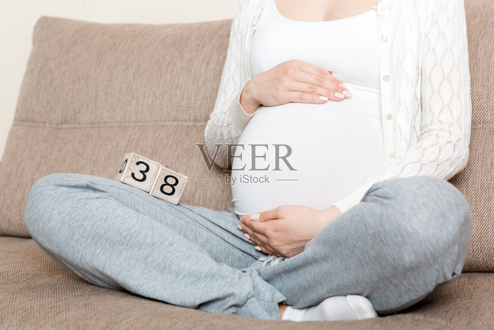 孕妇穿着白色内衣在家里的床上抱着日历带着38周的身孕。孕妇的概念。期待即将到来的宝宝照片摄影图片