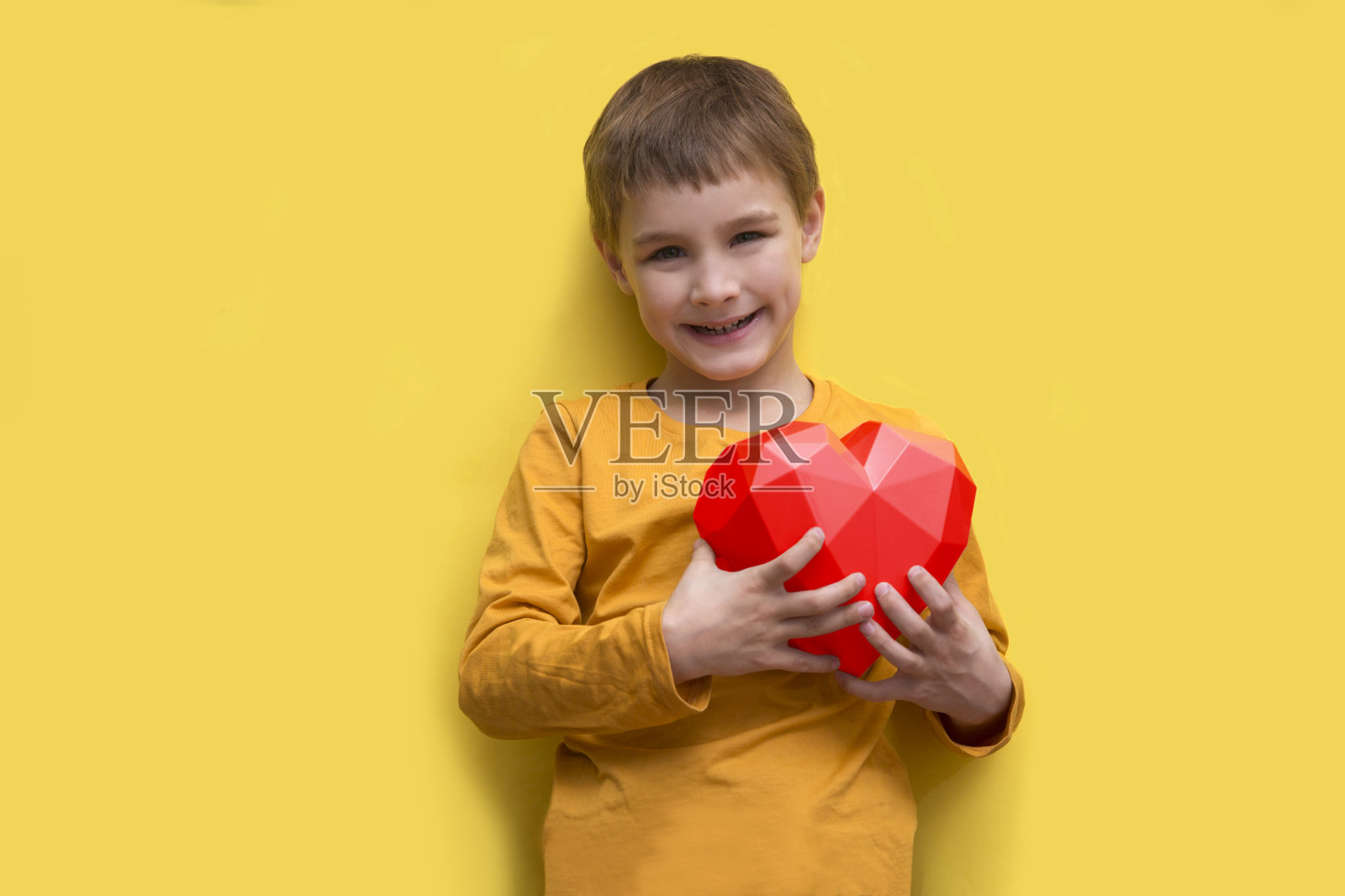 快乐的小男孩拿着一颗心在黄色的背景上。圣瓦伦丁的手法。横幅。副本的空间。妈妈的一天照片摄影图片
