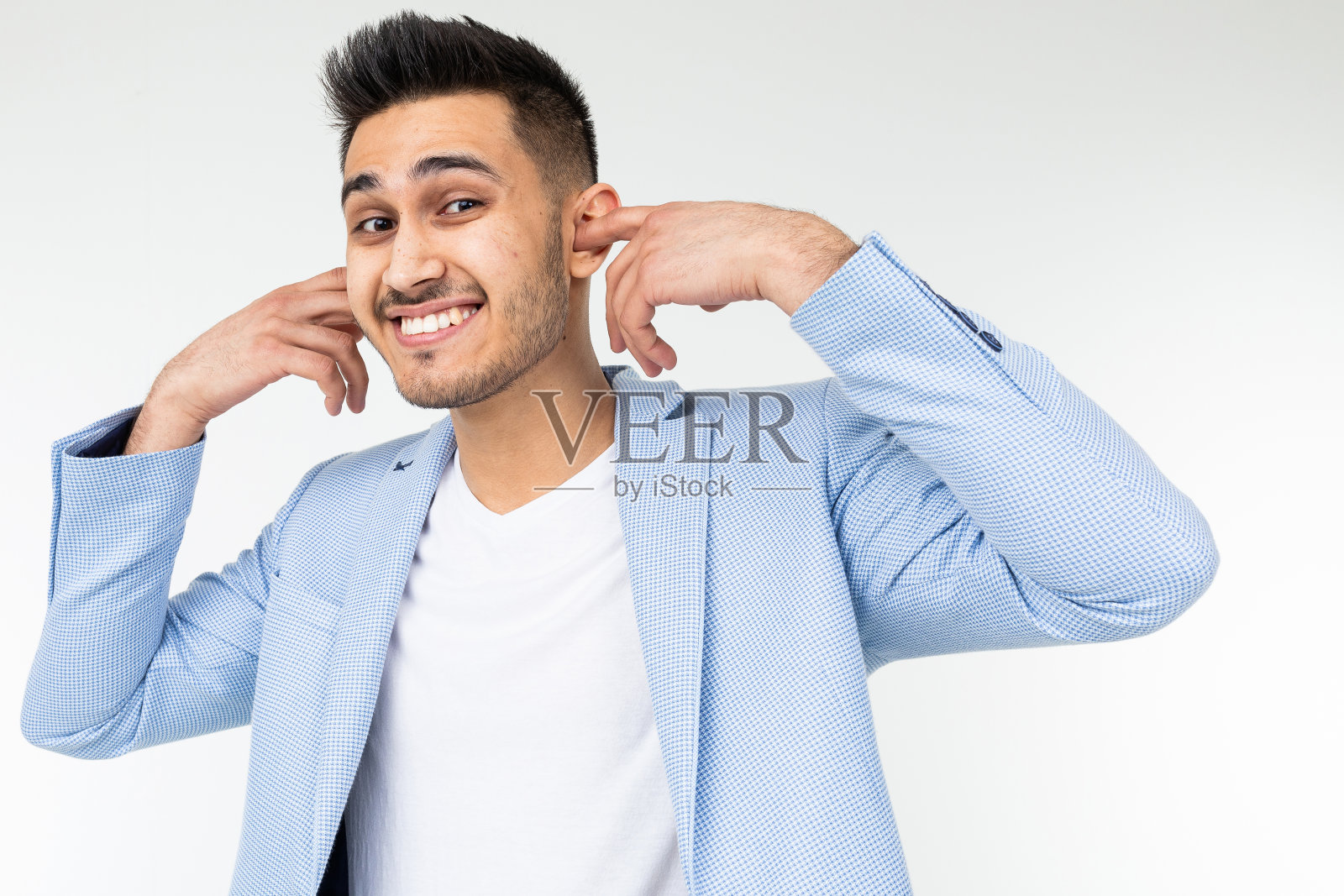 在白色背景下，一名身穿蓝色经典夹克的男子用手指堵住耳朵，以免噪音过大照片摄影图片