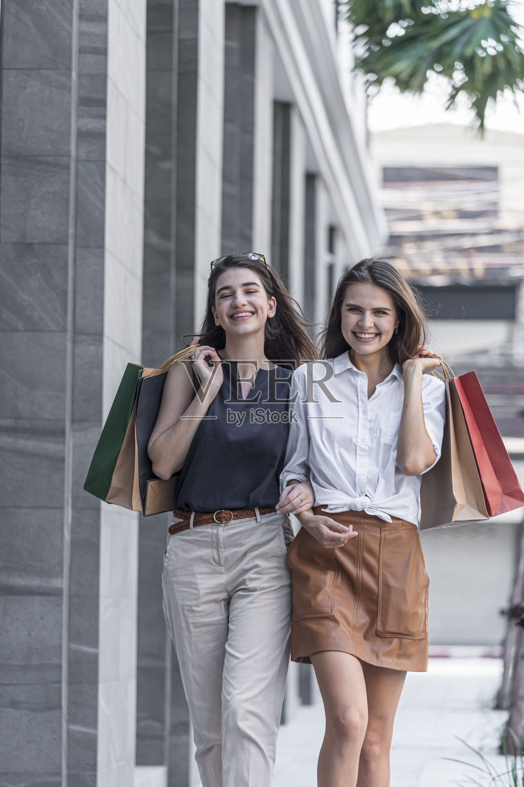年轻的购物狂朋友女性朋友走在街上，带着快乐和微笑的购物袋。照片摄影图片
