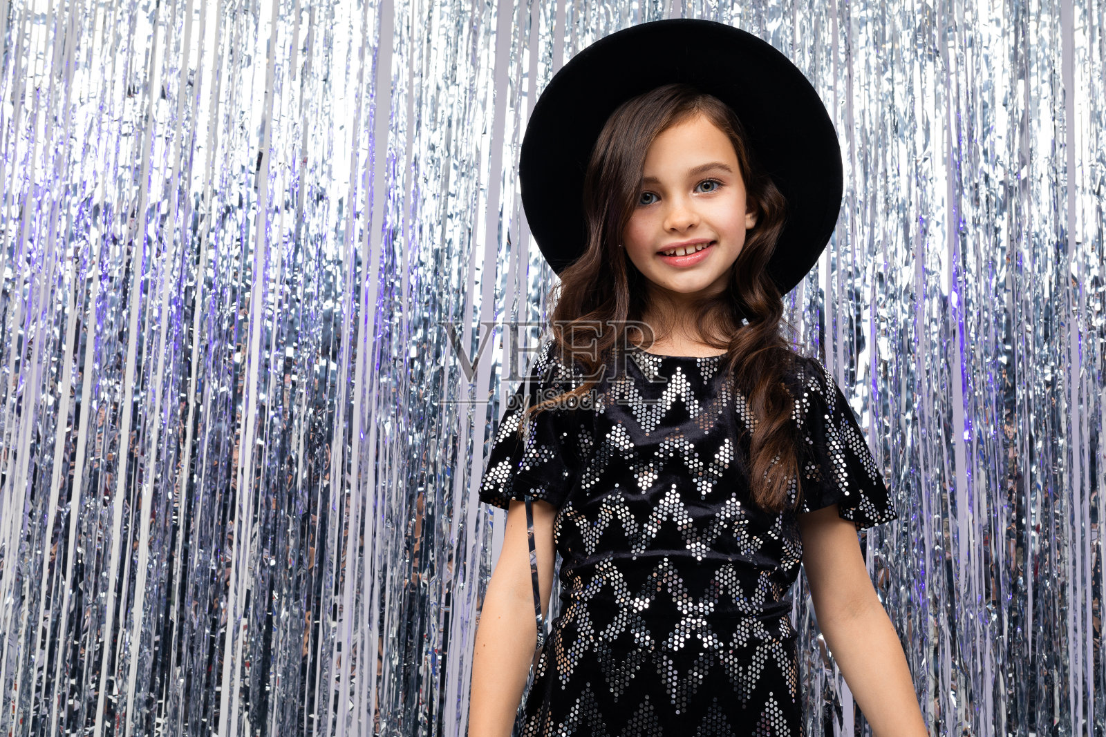 微笑的少女戴着黑色的帽子和优雅的服装在灿烂的雨的背景照片摄影图片