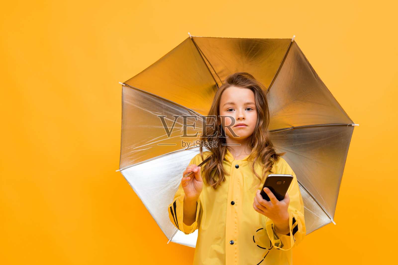 女孩坐在一把打开的伞下，坐在黄色的背景上讲电话照片摄影图片