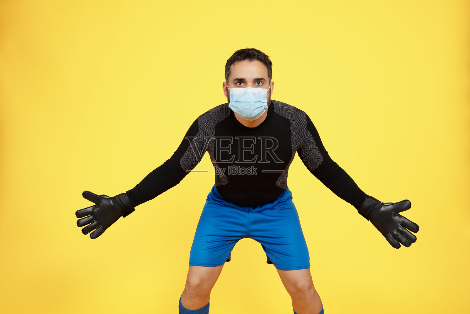 一名足球守门员在黄色背景下试图停下来，他脸上戴着口罩照片摄影图片