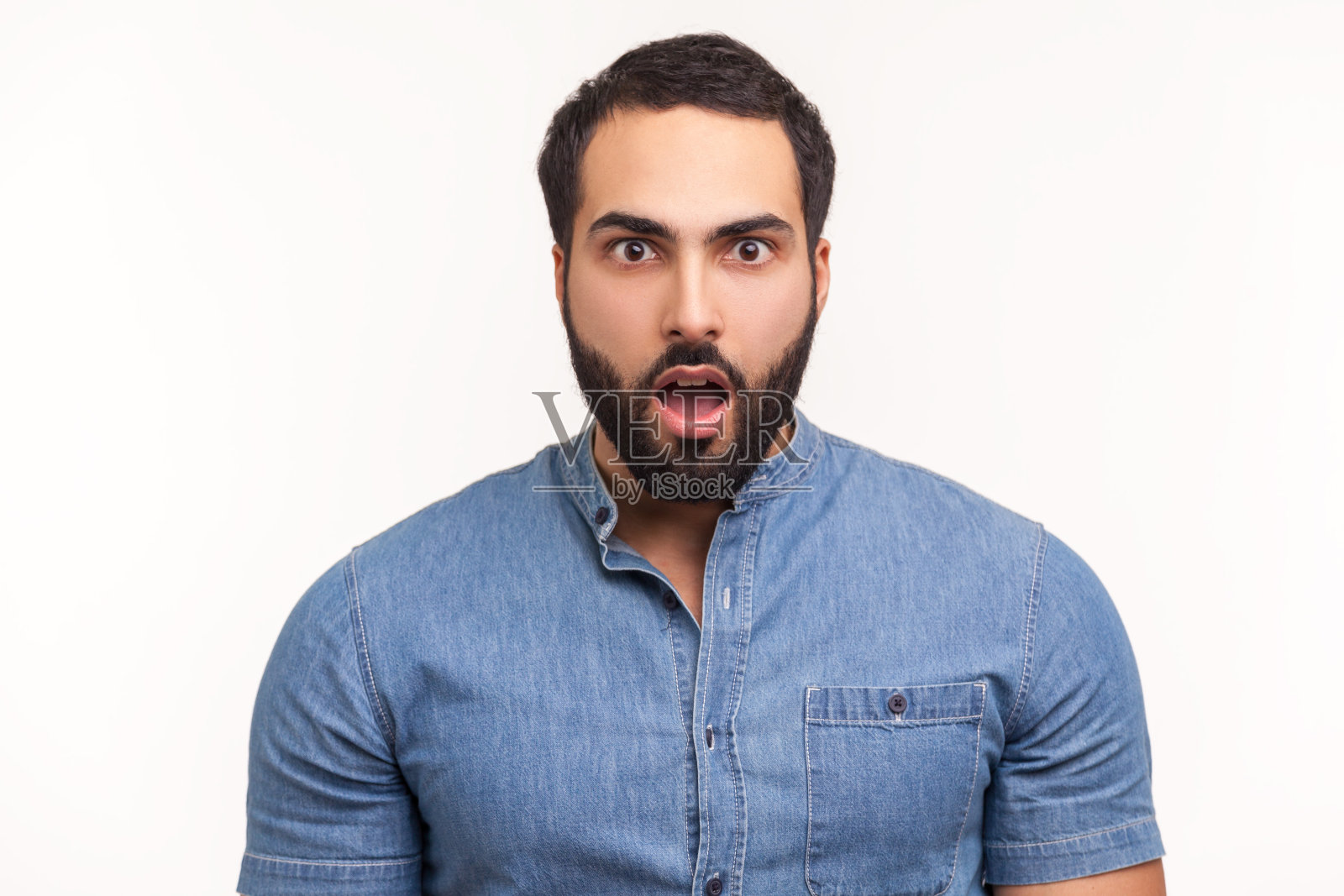 一个穿着蓝衬衫留着胡子的男人惊讶地睁大眼睛，张大嘴巴看着镜头，被意想不到的消息震惊了照片摄影图片