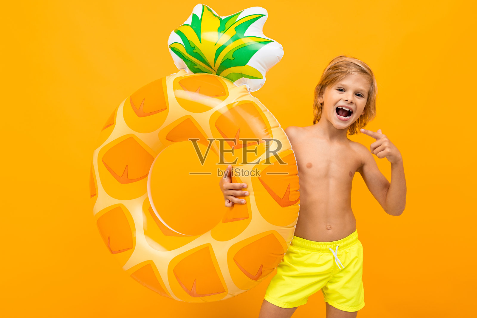 英俊的男孩在泳裤持有一个橡胶圈，微笑和手势孤立在橙色的背景照片摄影图片