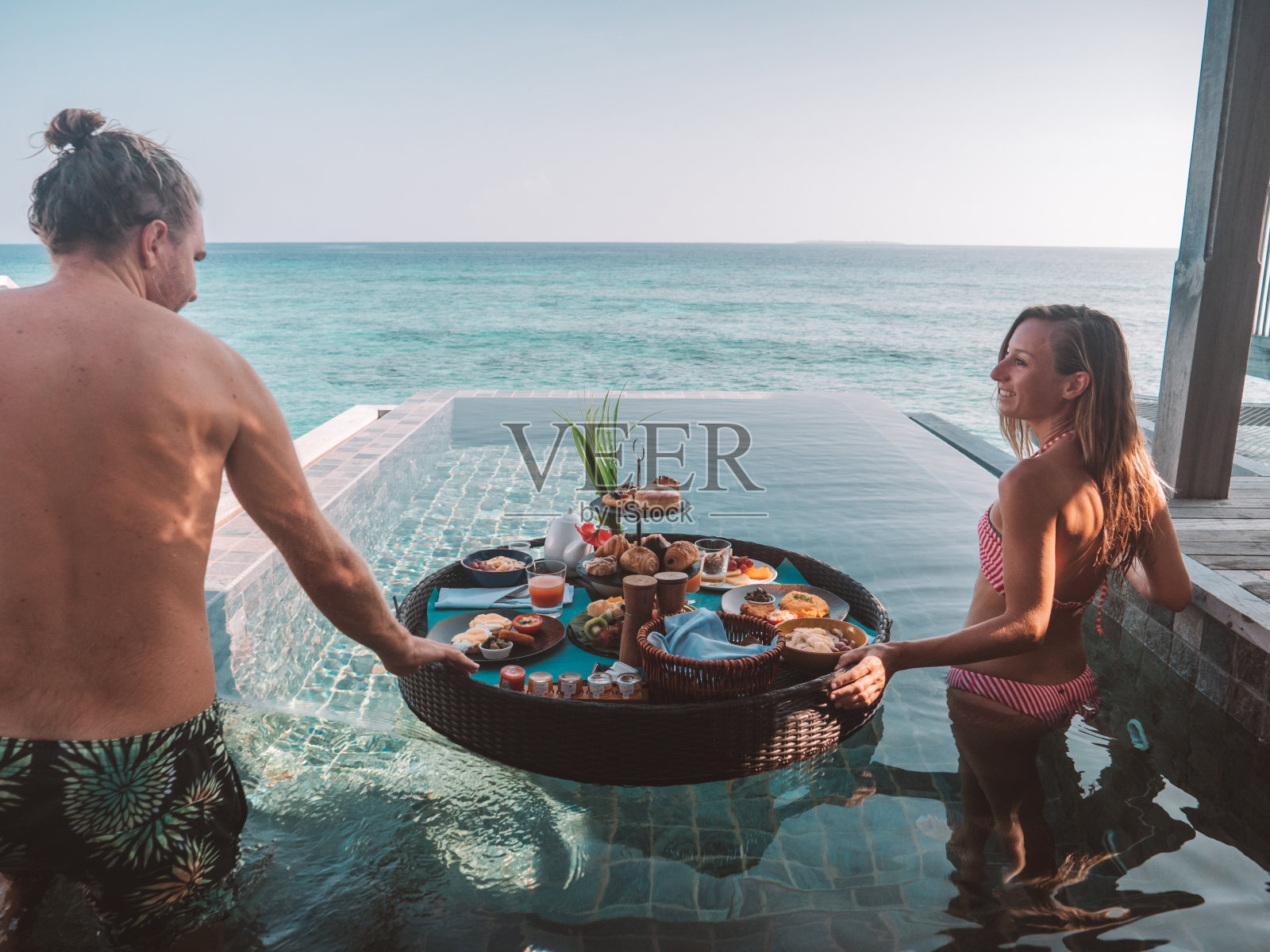 一对可爱的情侣在私人泳池别墅享受漂浮早餐照片摄影图片