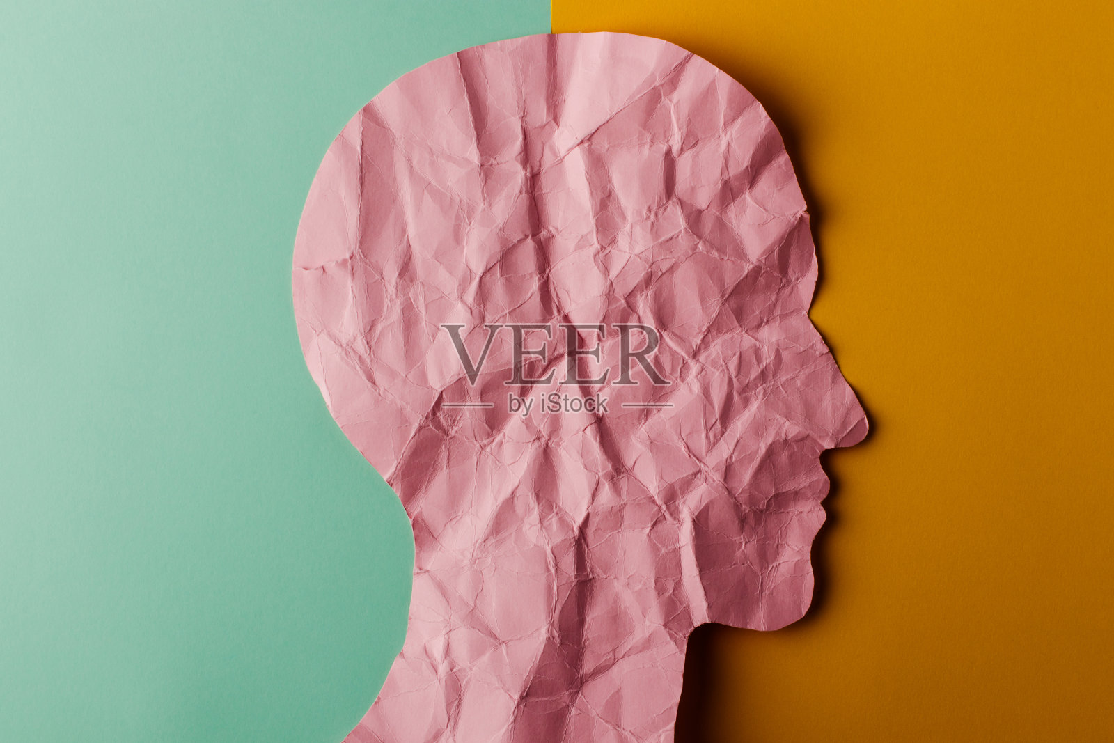 纸做的头像剪影。皱巴巴的粉色纸，形状像一个人的头，绿色和黄色的纸背景上有拷贝空间。照片摄影图片