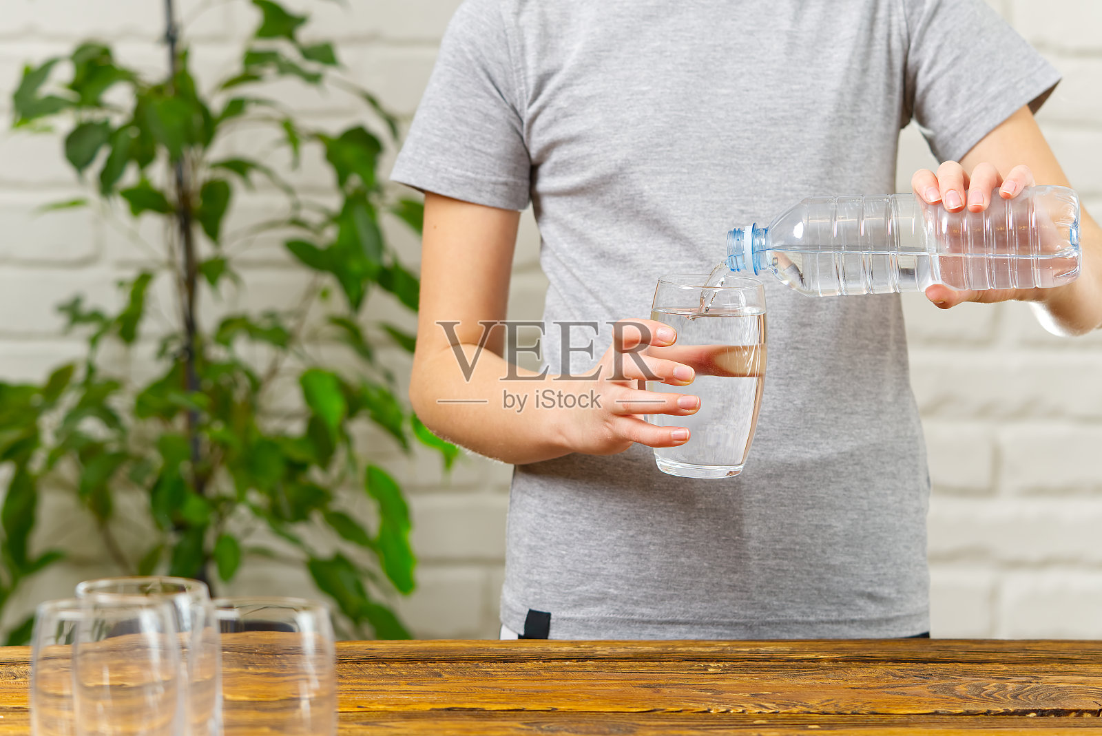 女孩正把塑料瓶里的水倒进木桌上的玻璃杯里照片摄影图片