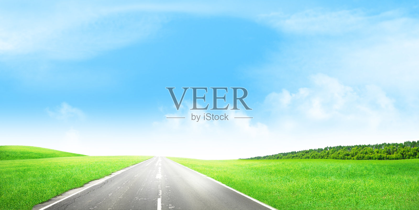 道路穿过绿色的草地和阳光灿烂的天空照片摄影图片