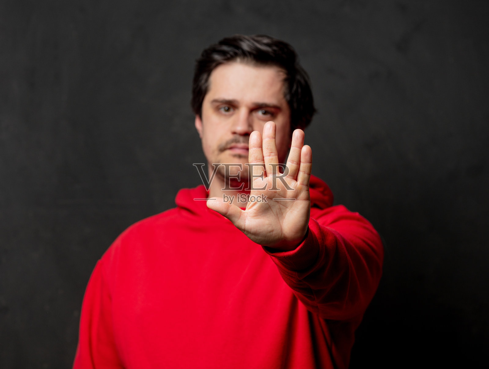 穿红色运动衫的白人在黑色背景上显示火神敬礼照片摄影图片