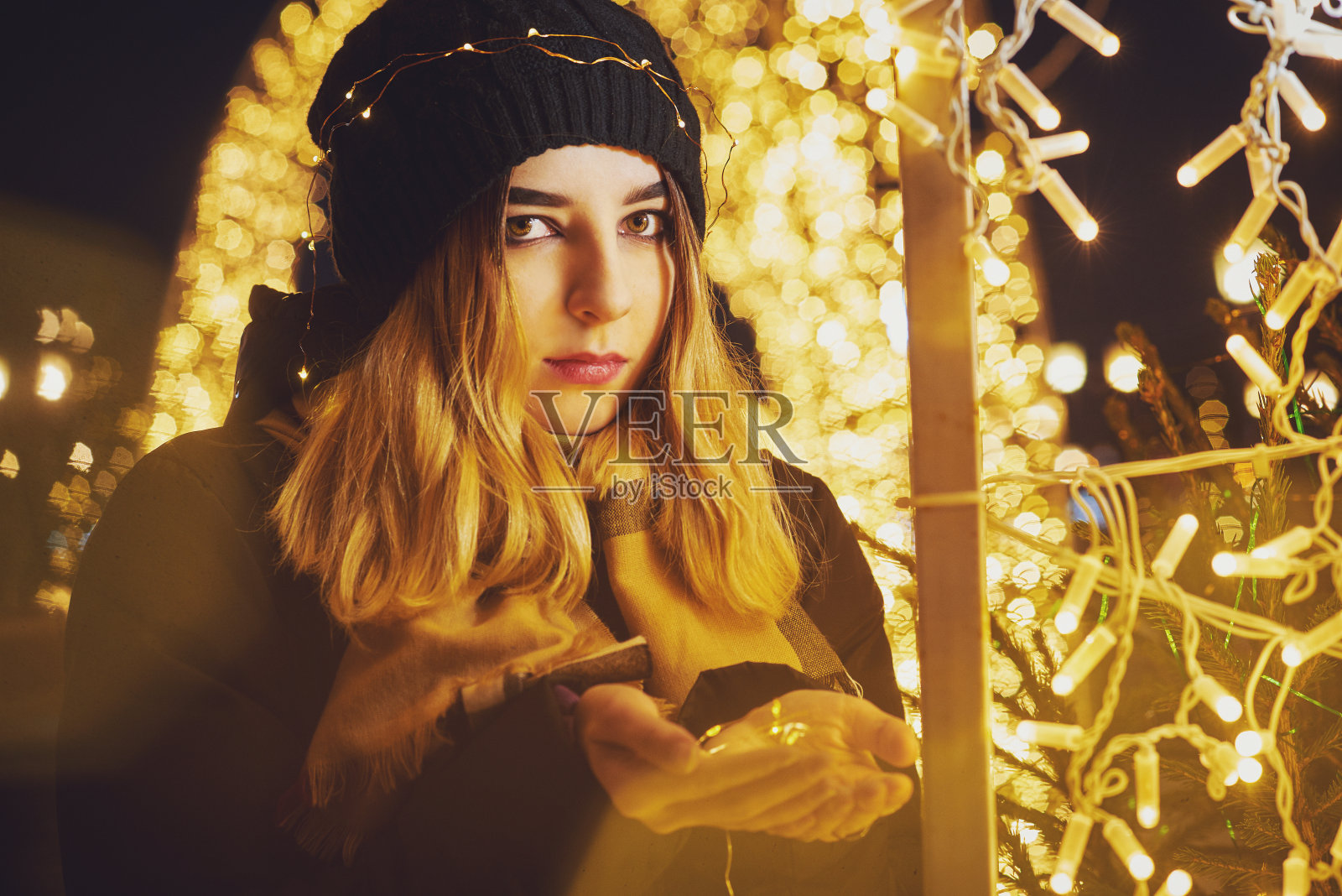 女孩在夜晚的灯光背景上戴着一个灯泡花环。城市的节日灯光照片摄影图片