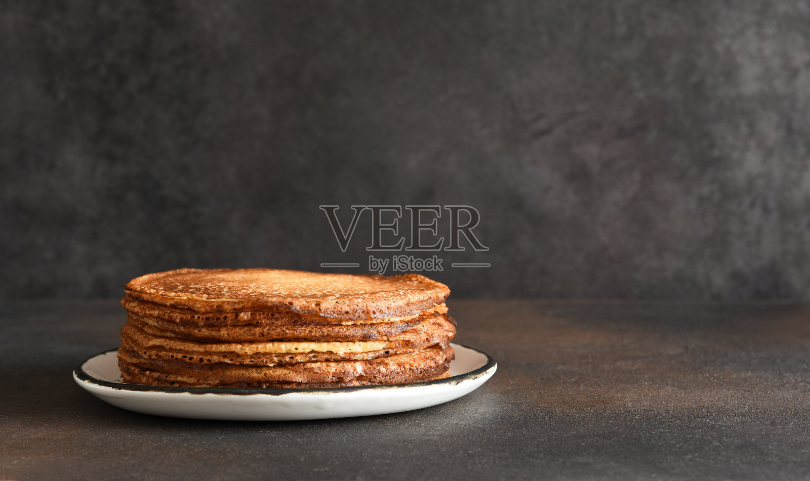 在深色背景上的盘子上的煎饼堆。薄煎饼。早上好。照片摄影图片