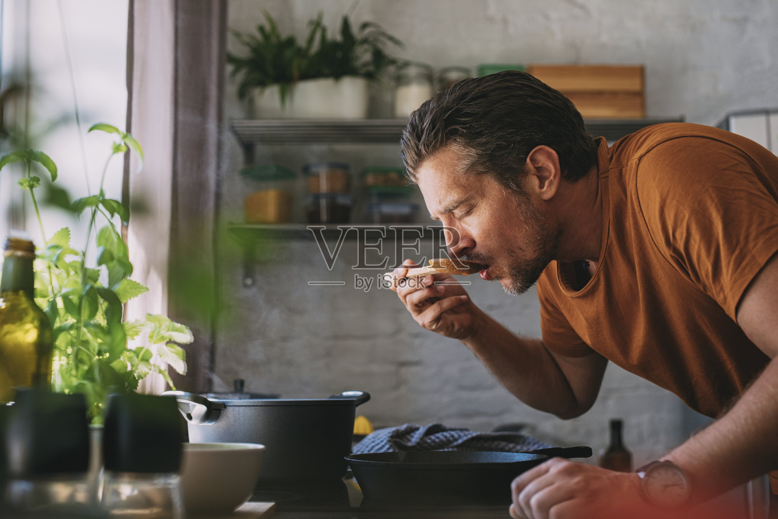 英俊的年轻人在厨房里用调羹品尝酱汁照片摄影图片