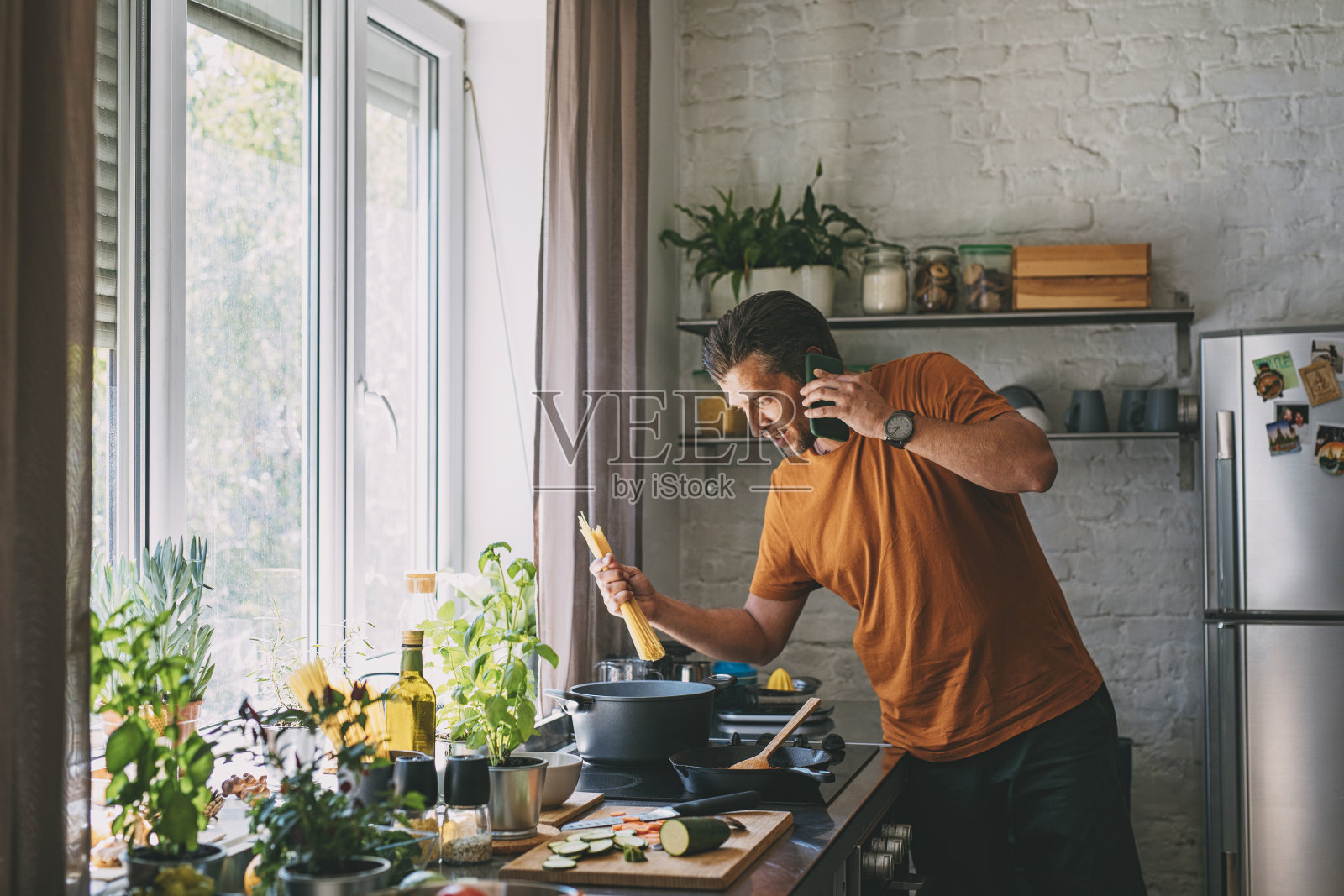 英俊的年轻人在家里准备意大利面时打电话照片摄影图片
