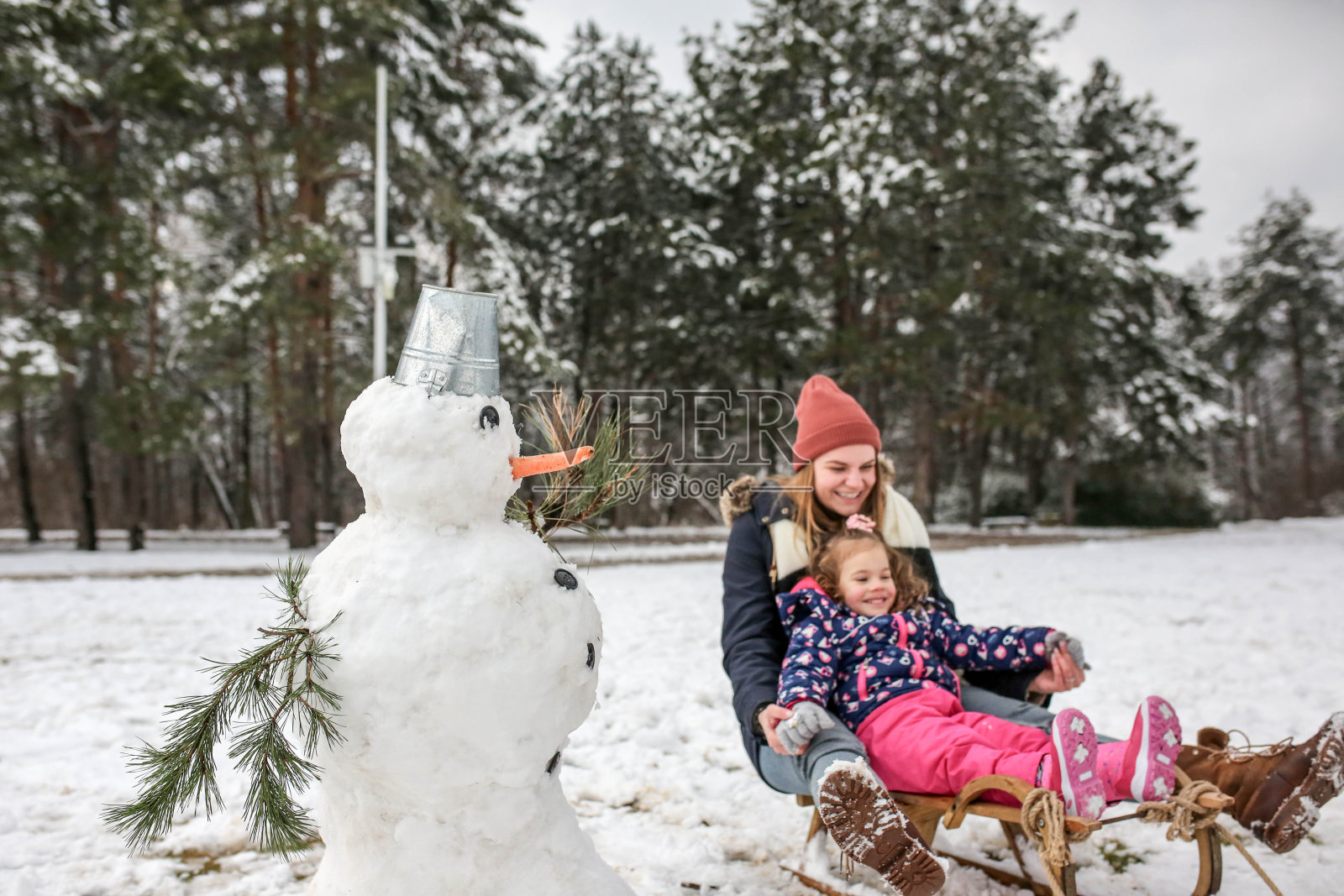 母亲和女儿在一个寒冷的冬天拉雪橇和堆雪人照片摄影图片
