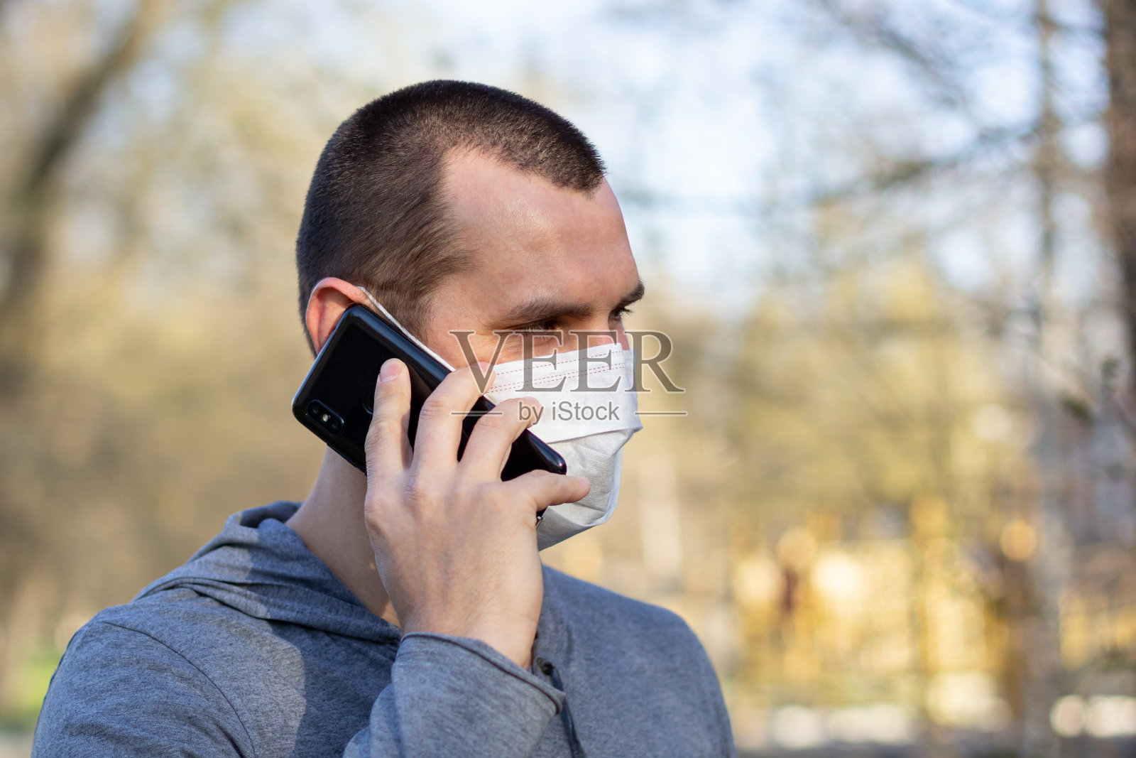 一个戴着医用口罩的白人正在打电话。在户外街道免受病毒感染。照片摄影图片