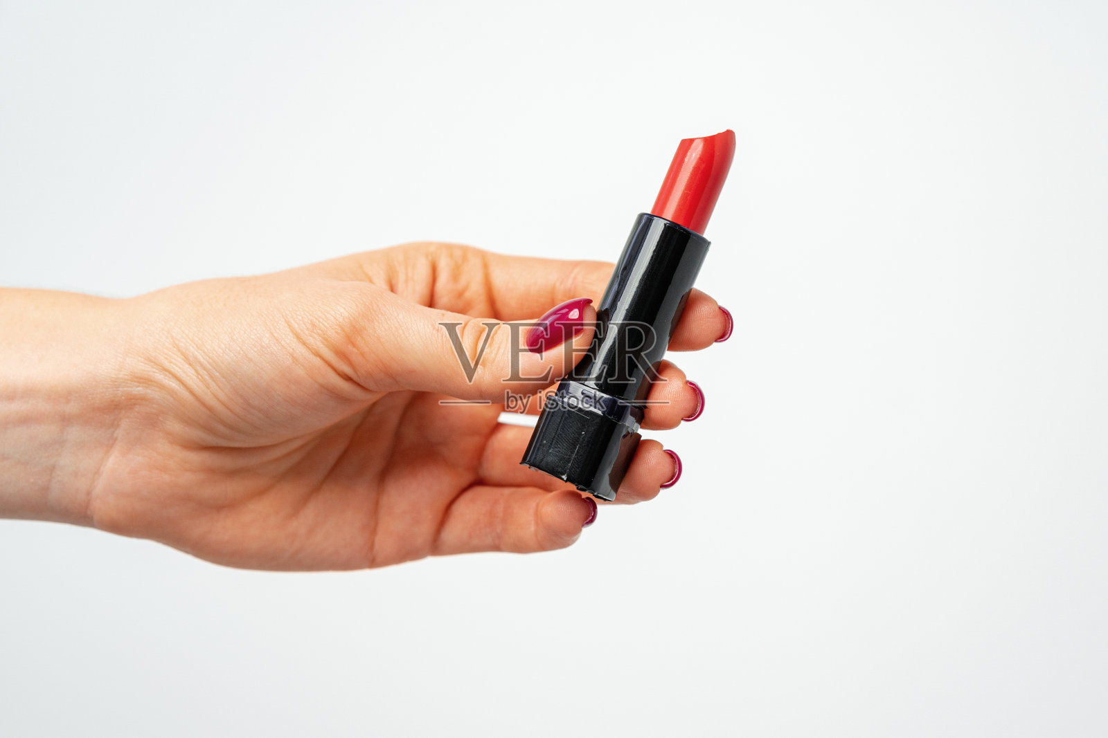 灰色背景下，女性手握红色唇膏照片摄影图片