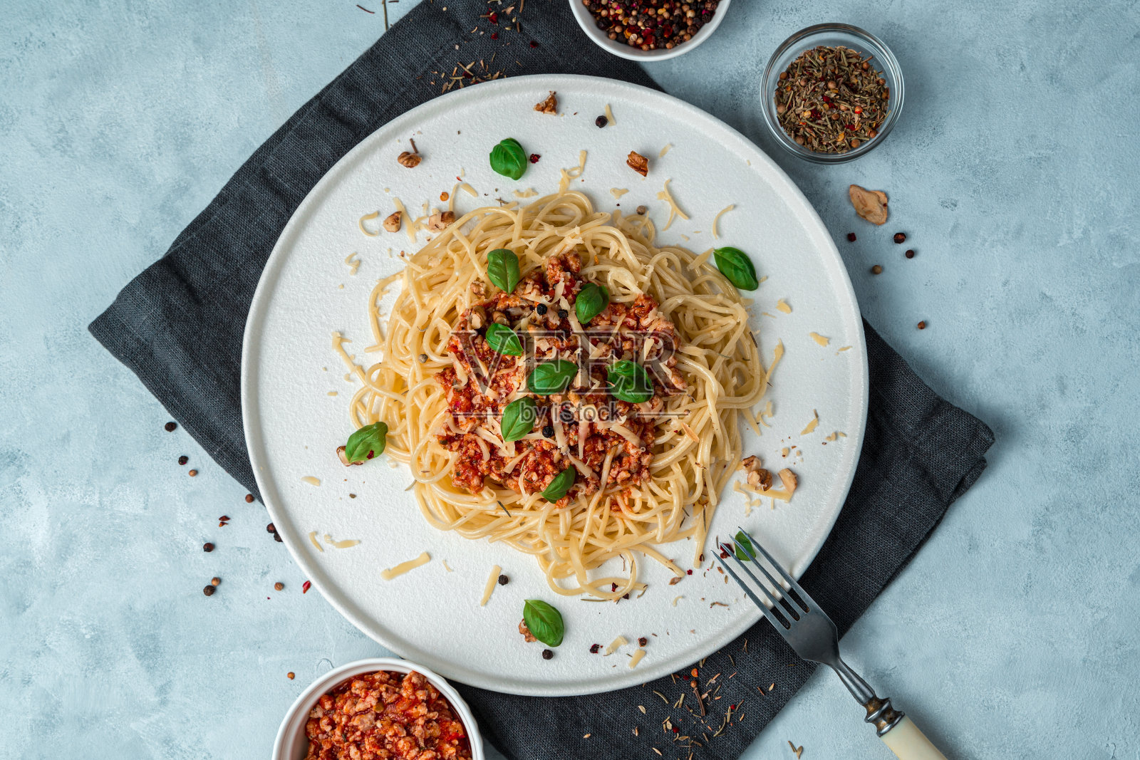 在灰色背景的平底盘子里放意大利面和番茄酱，配上肉末、罗勒叶、奶酪和坚果照片摄影图片