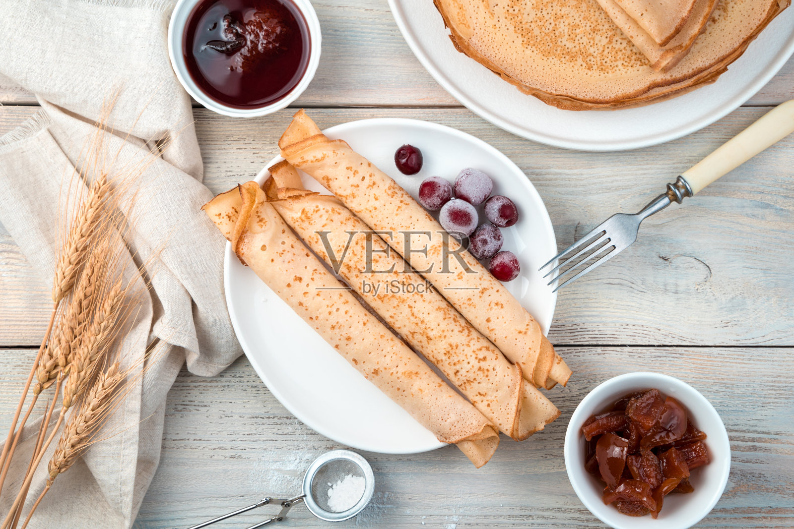 三个煎饼卷进一个管子里，还有冰冻的浆果放在餐桌上的一个白色盘子里照片摄影图片