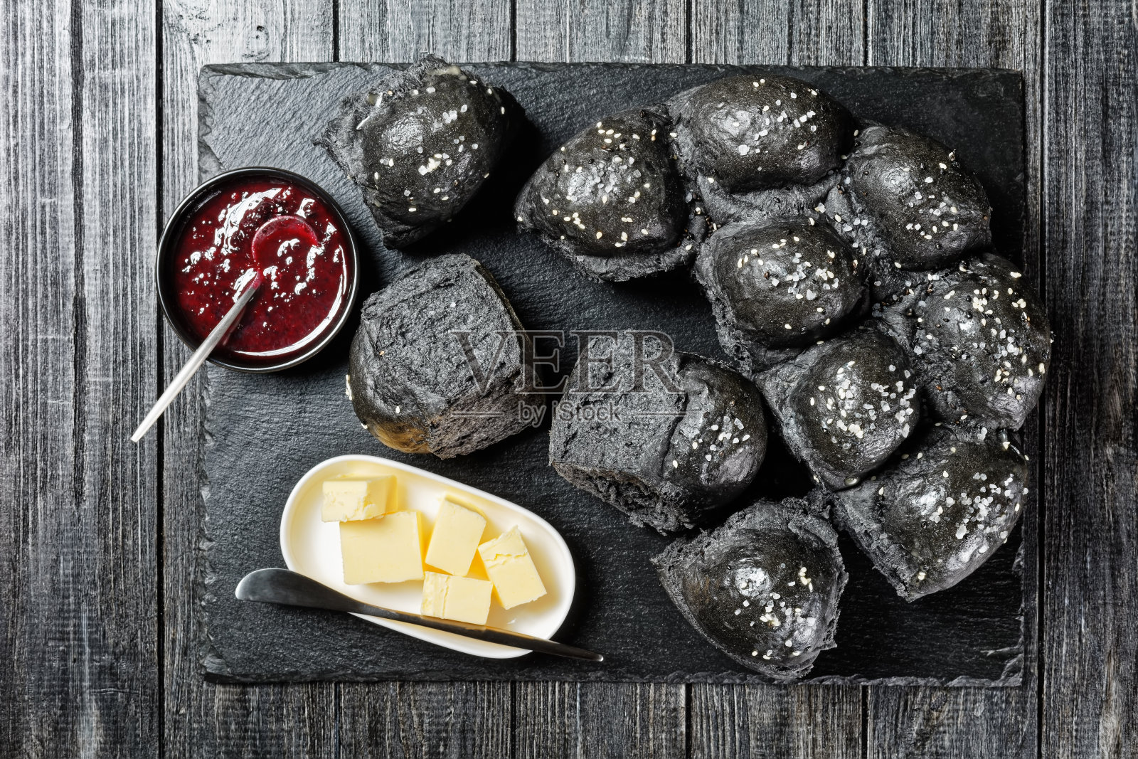 上面撒着海盐的黑面包由活性炭酵母面团制成，放在黑色的石板上，黑色的木桌上，还有黄油和蔓越莓果酱照片摄影图片