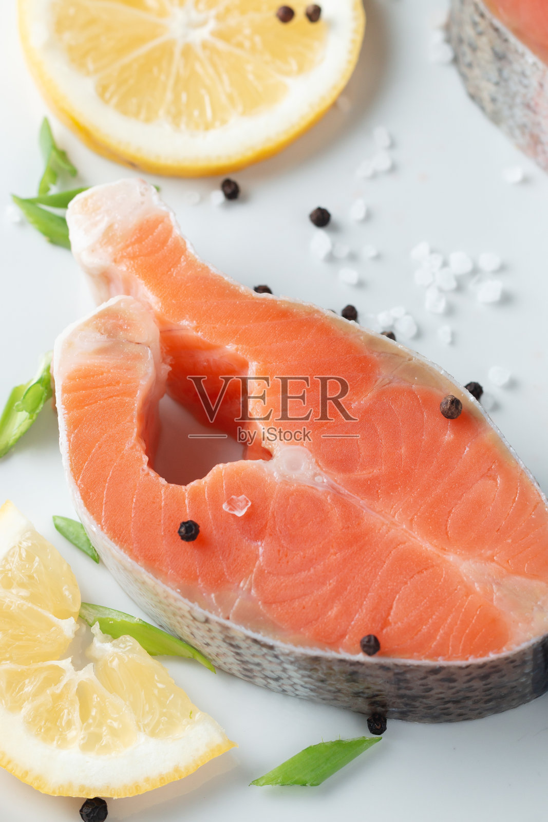 鲜嫩多汁的三文鱼排放在白色盘子里，配以洋葱、柠檬和香料，放在天然石板桌上，特写。美味的三文鱼片。照片摄影图片